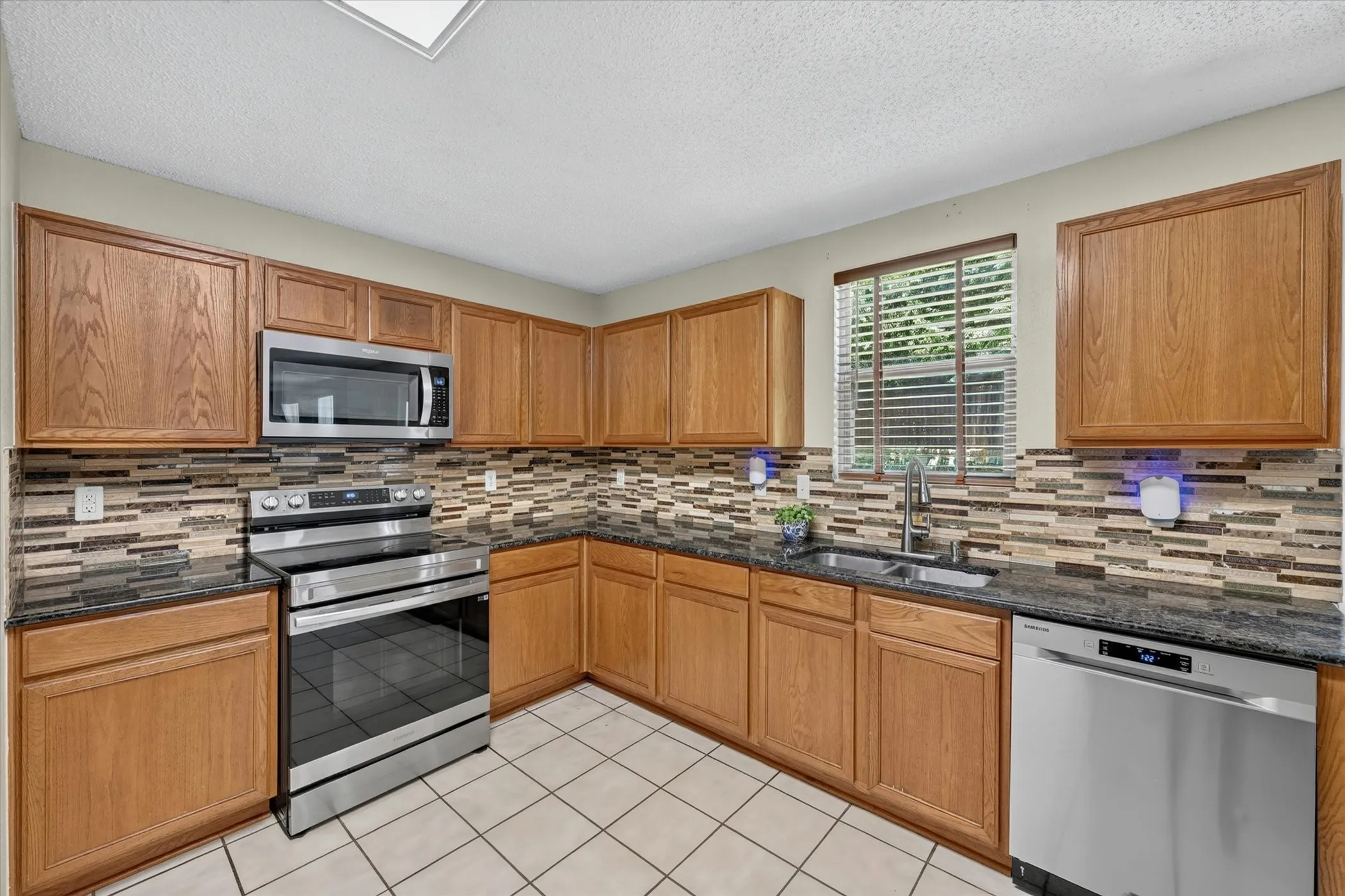 Kitchen featuring wood cabinetry, dark countertops, a mosaic tile backsplash, stainless steel appliances, and tile flooring