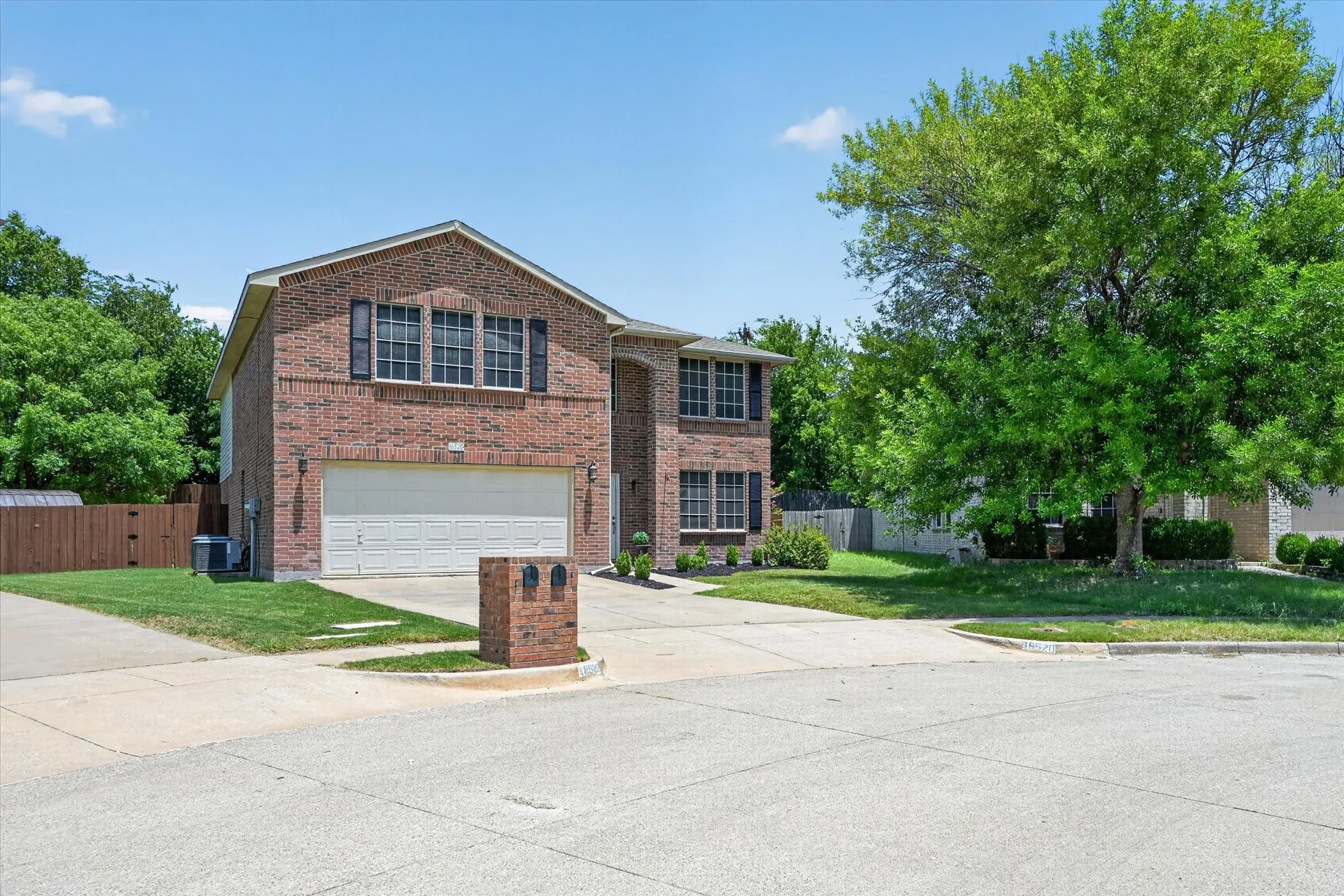 Brick exterior featuring a two-car garage and black louvered shutters