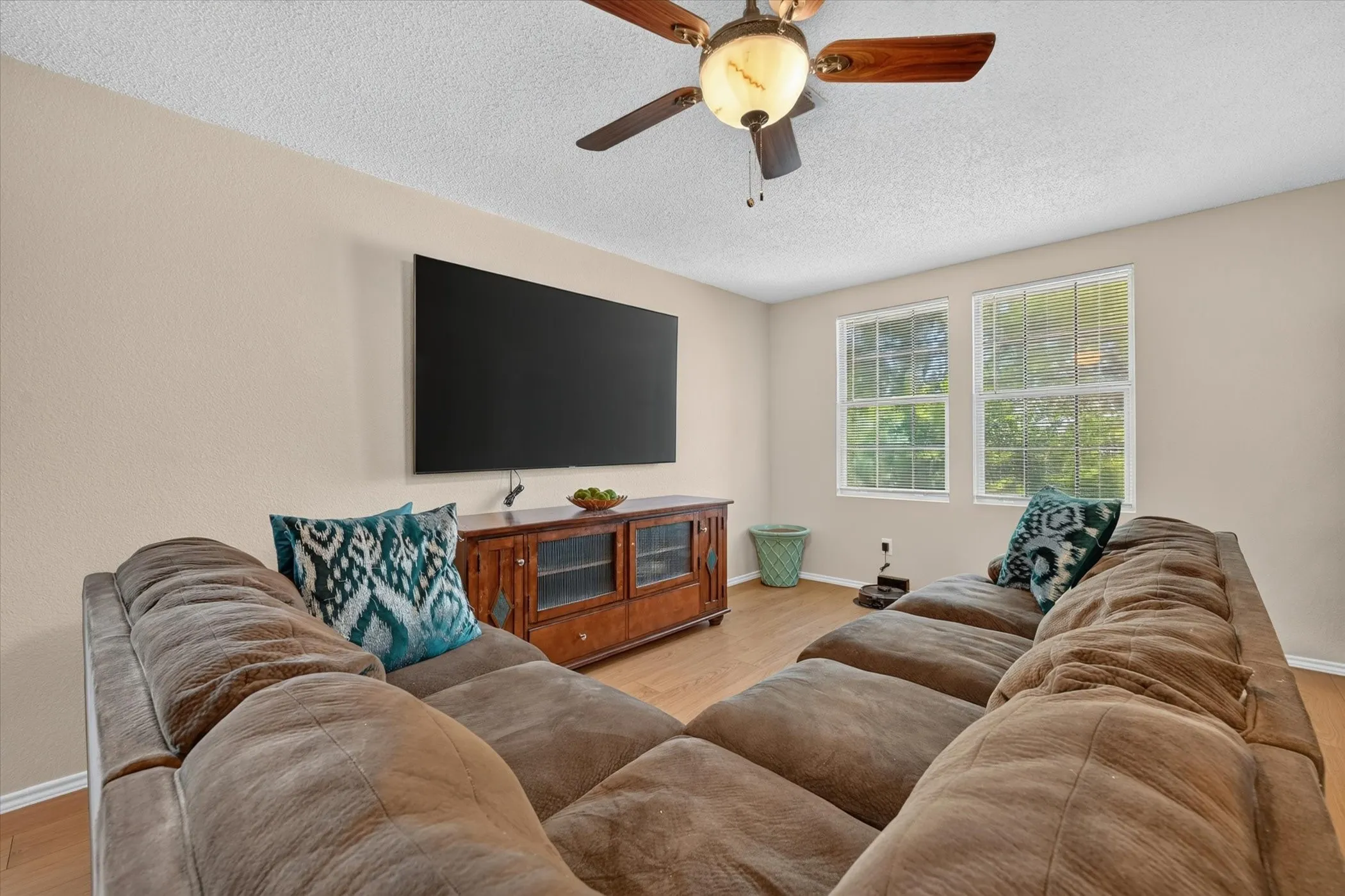 Living area featuring wood-finish flooring, two window openings, and a ceiling fan with integrated lighting