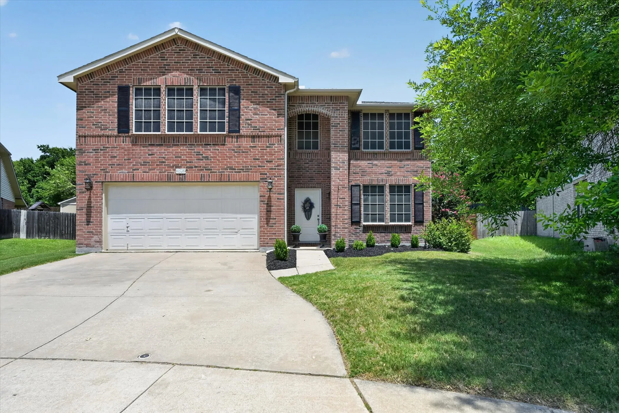 Brick facade property featuring an arched entryway, multiple windows with dark shutters, a two-car garage, and a concrete driveway