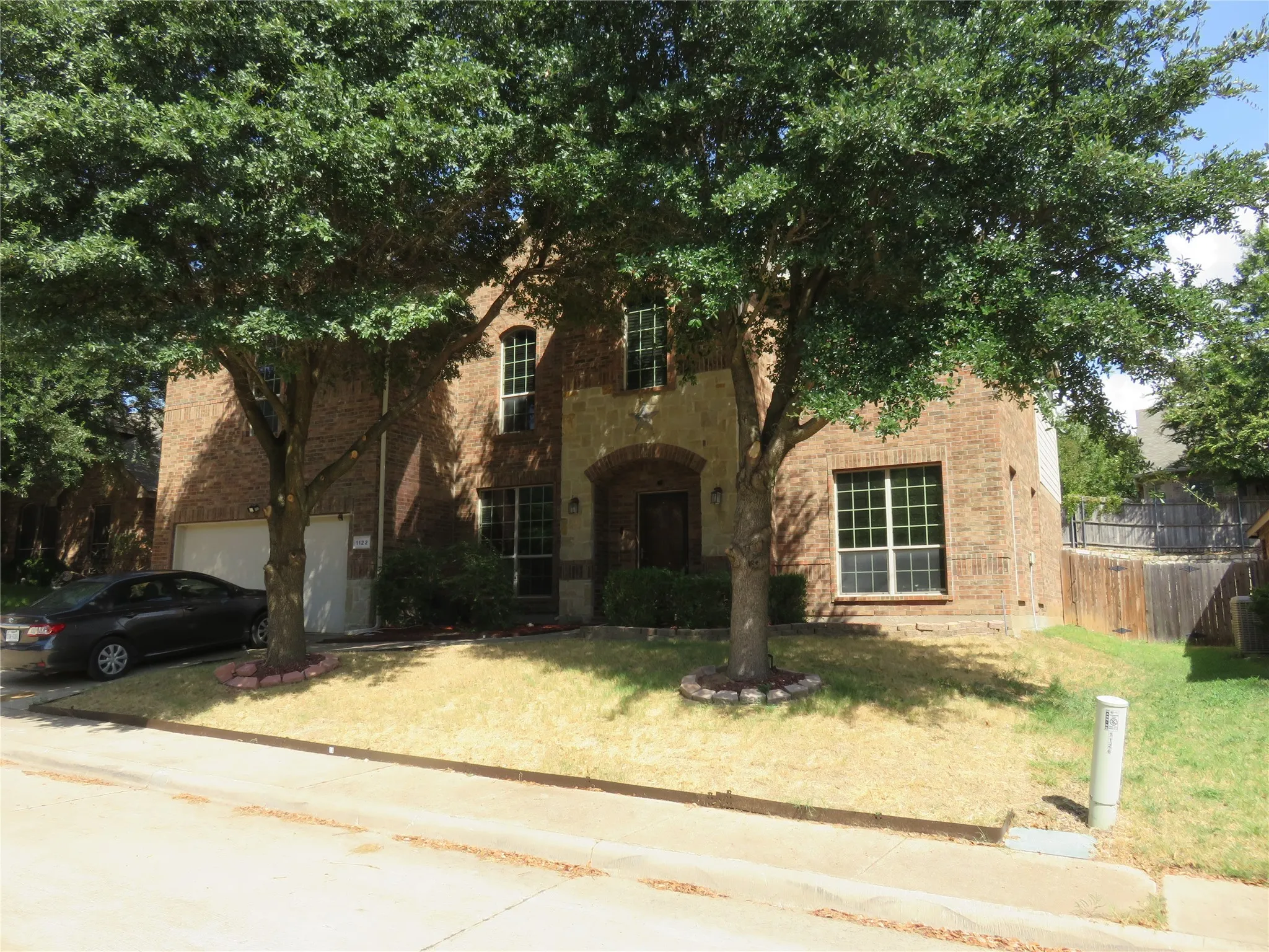 Brick exterior with stone accents, arched entryway, attached garage, and mature trees