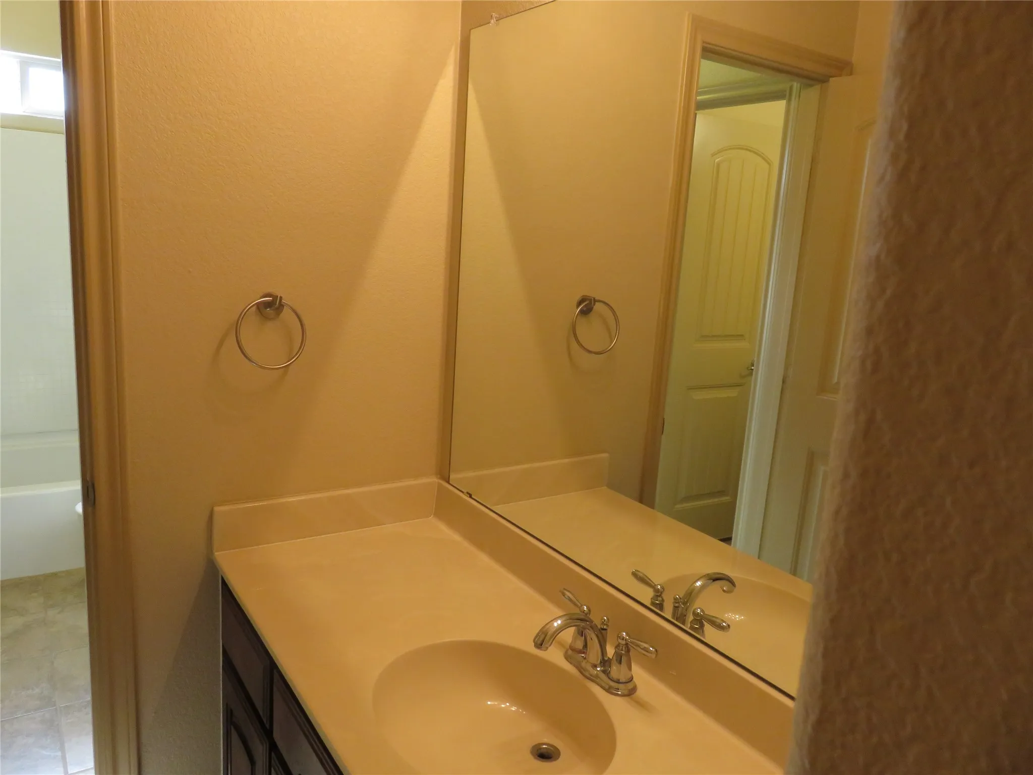 Vanity with integrated sink, chrome faucet, and expansive wall-mounted mirror
