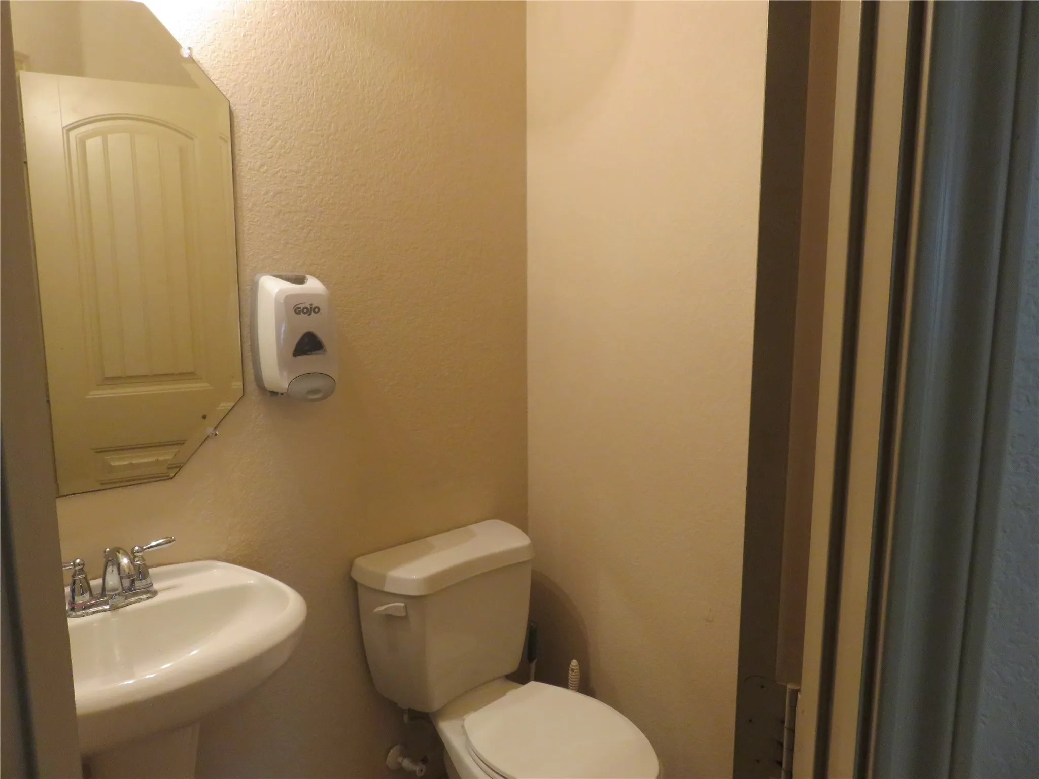 Pedestal sink with chrome fixtures, an octagonal mirror, and a white toilet
