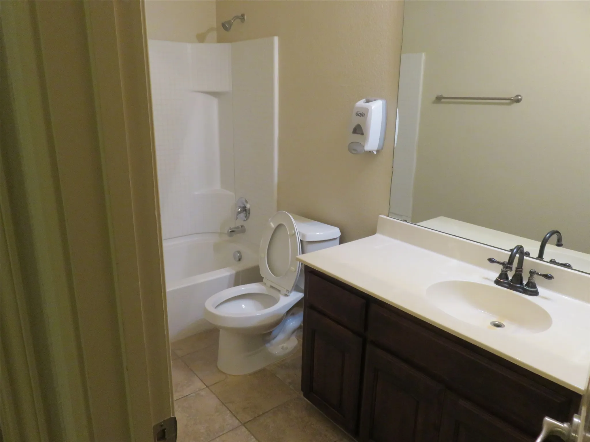 Bathroom featuring a dark wood-finish vanity with an integrated sink, a large wall mirror, and a white bathtub with an overhead shower