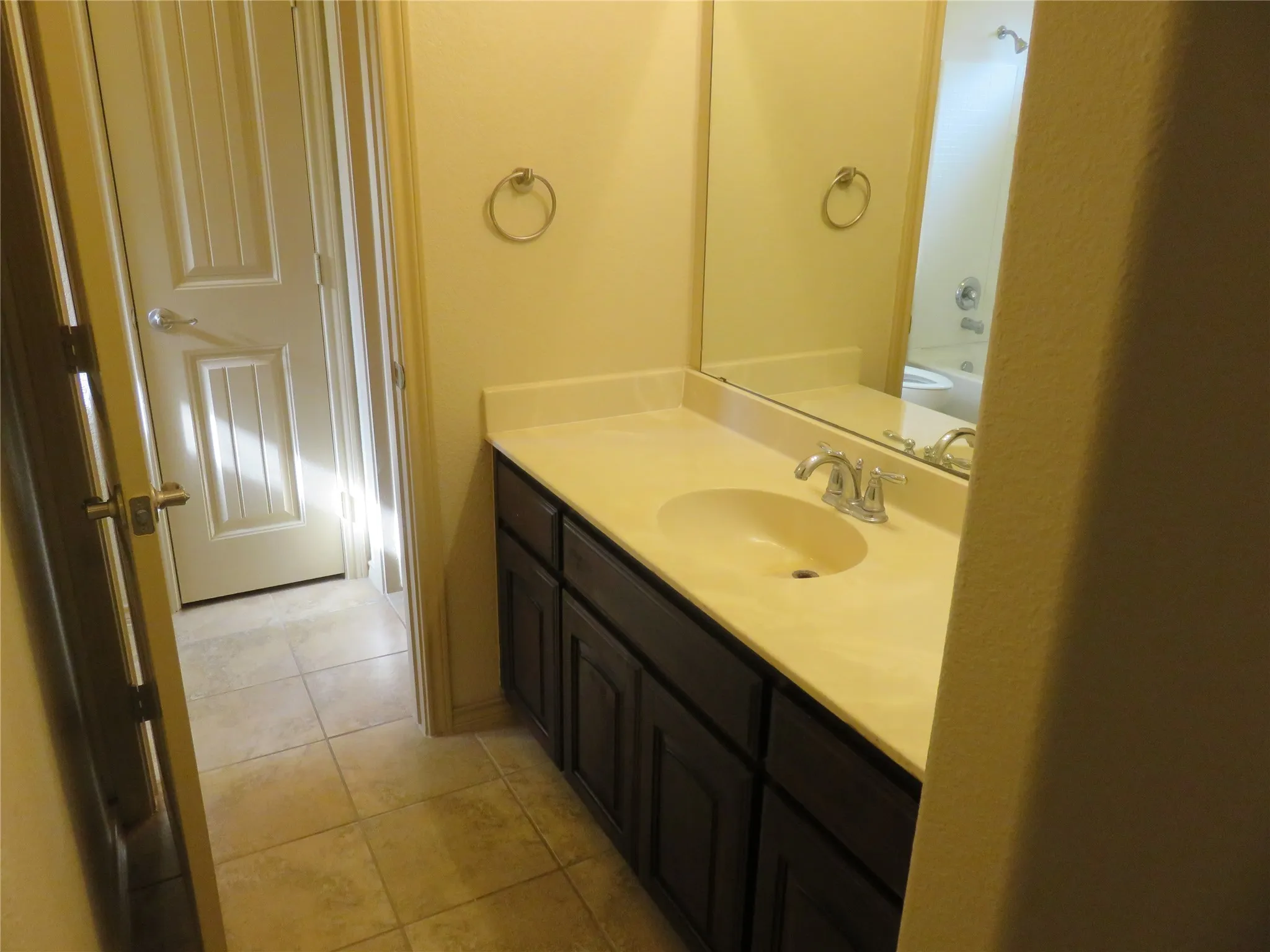 Bathroom vanity featuring a light-toned countertop with integrated sink, dark wood-finish cabinetry, and an expansive wall mirror