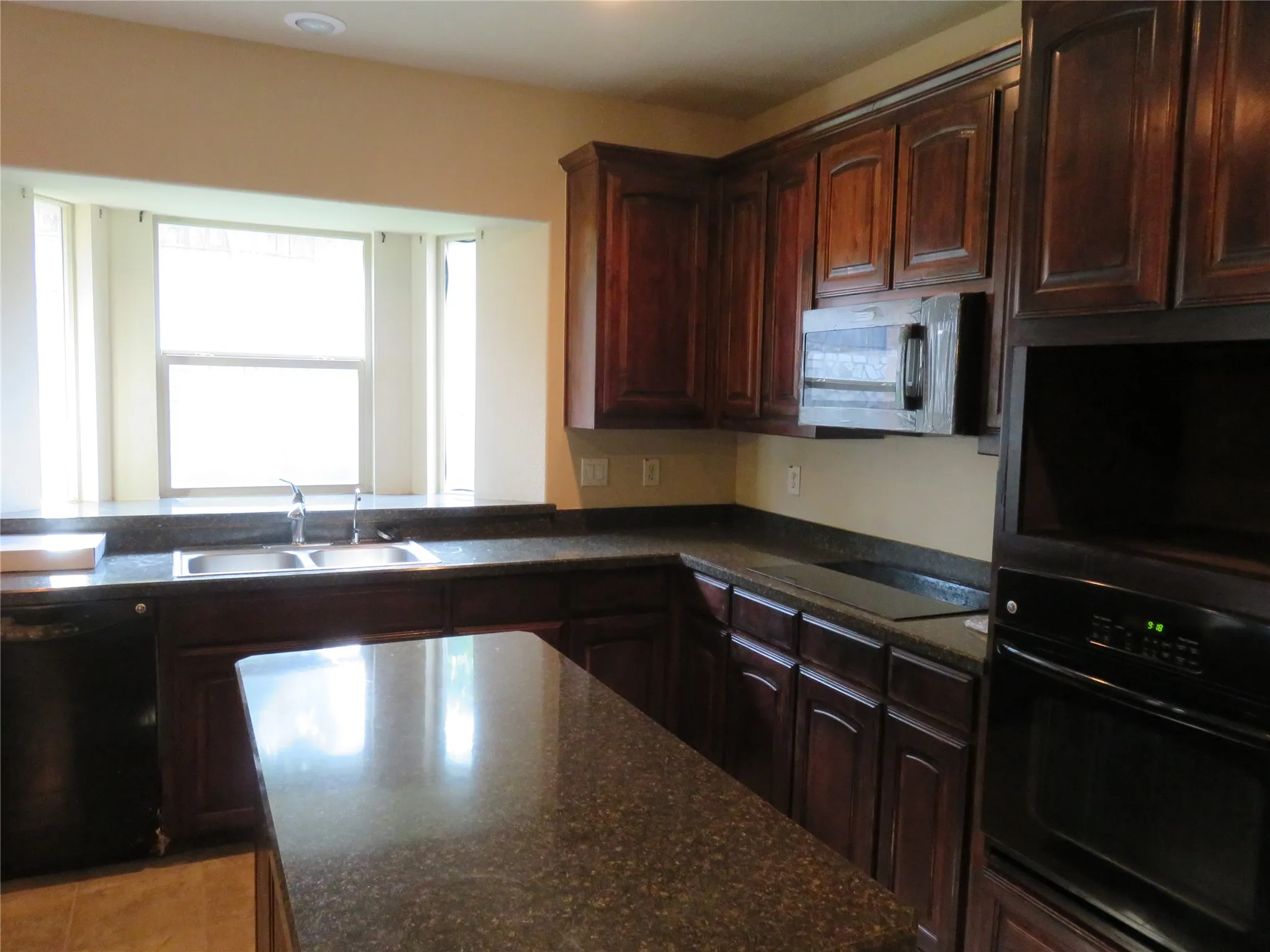 Kitchen featuring dark wood cabinetry, a built-in oven, integrated microwave, and a black cooktop