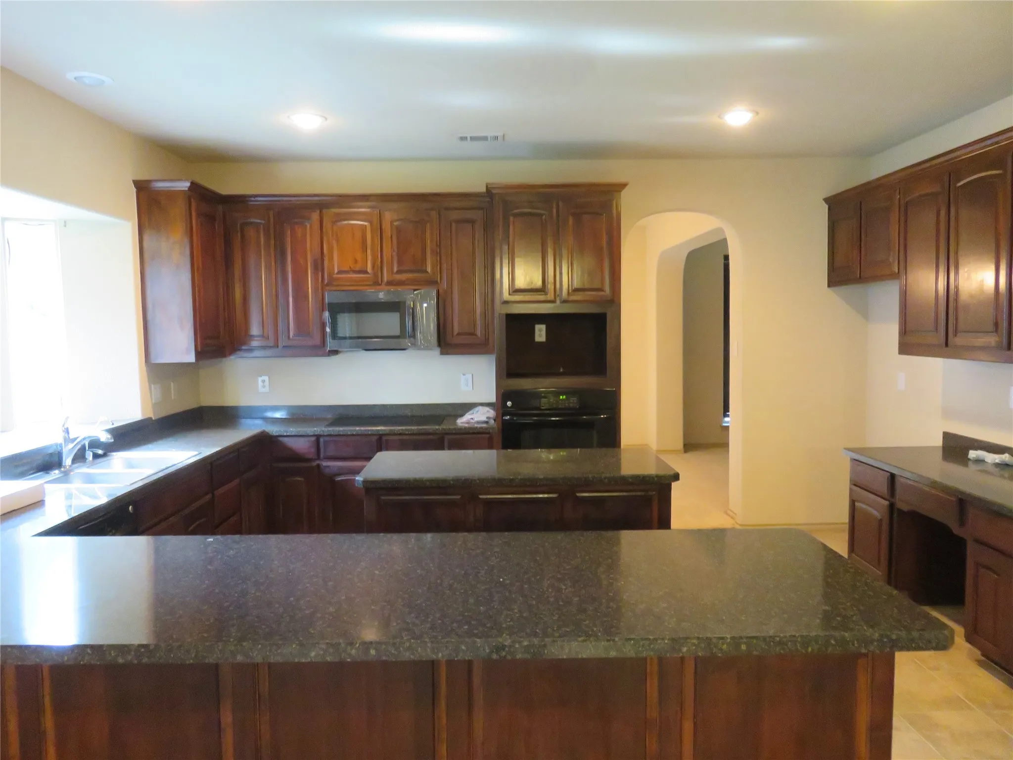 Spacious kitchen featuring rich wood cabinetry, dark speckled countertops, a built-in microwave, and recessed ceiling lighting
