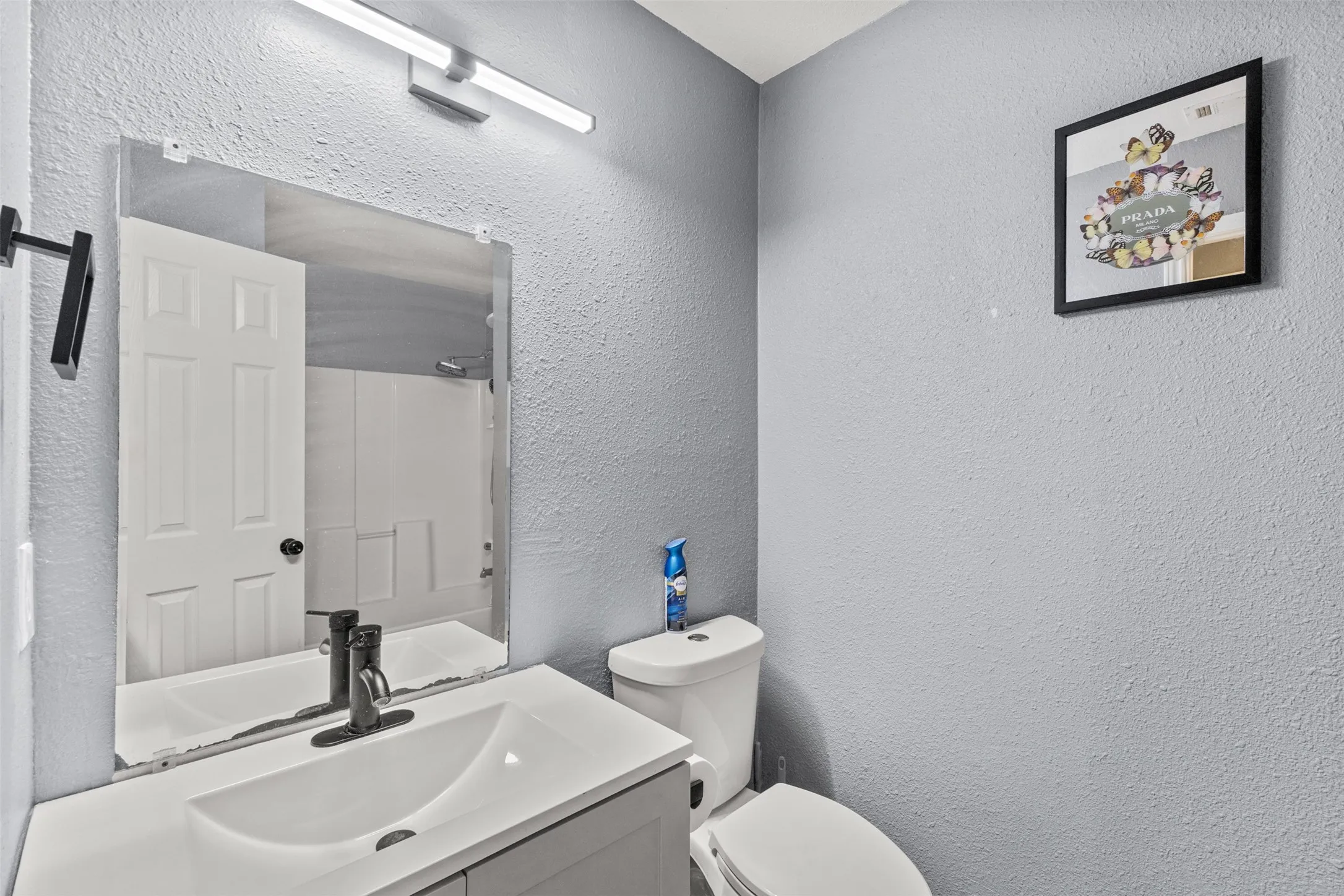 Bathroom featuring a white vanity with an integrated sink, black faucet, wall-mounted mirror, and overhead linear light fixture