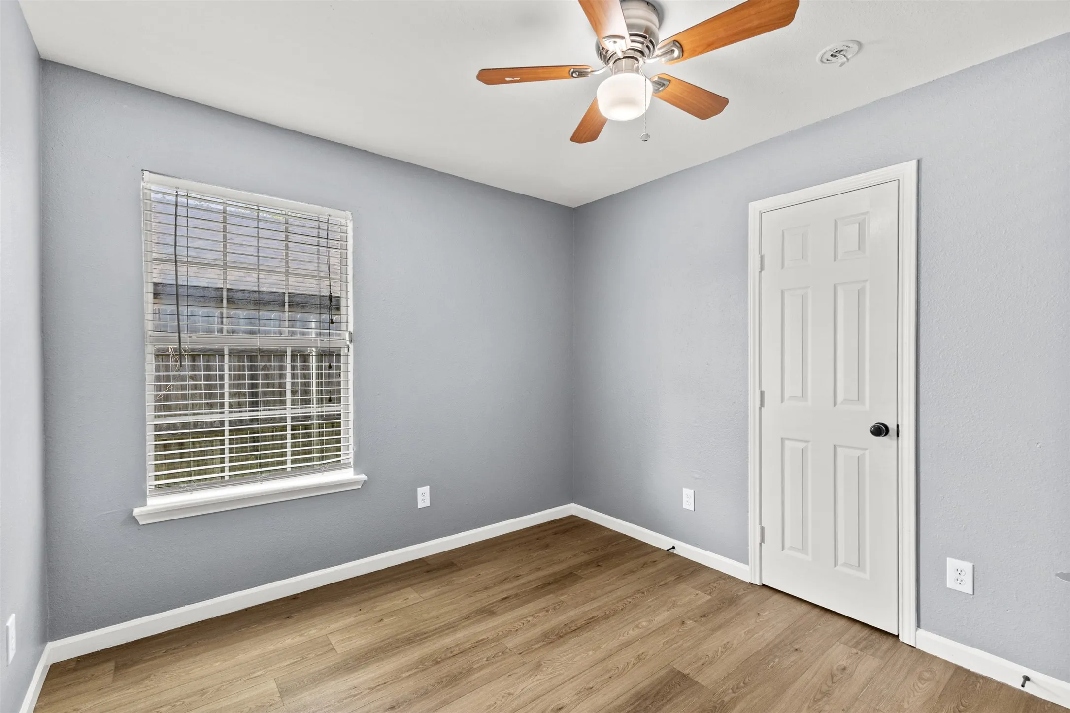 Room featuring wood-finish flooring, a ceiling fan with light fixture, light gray wall paint, and white trim
