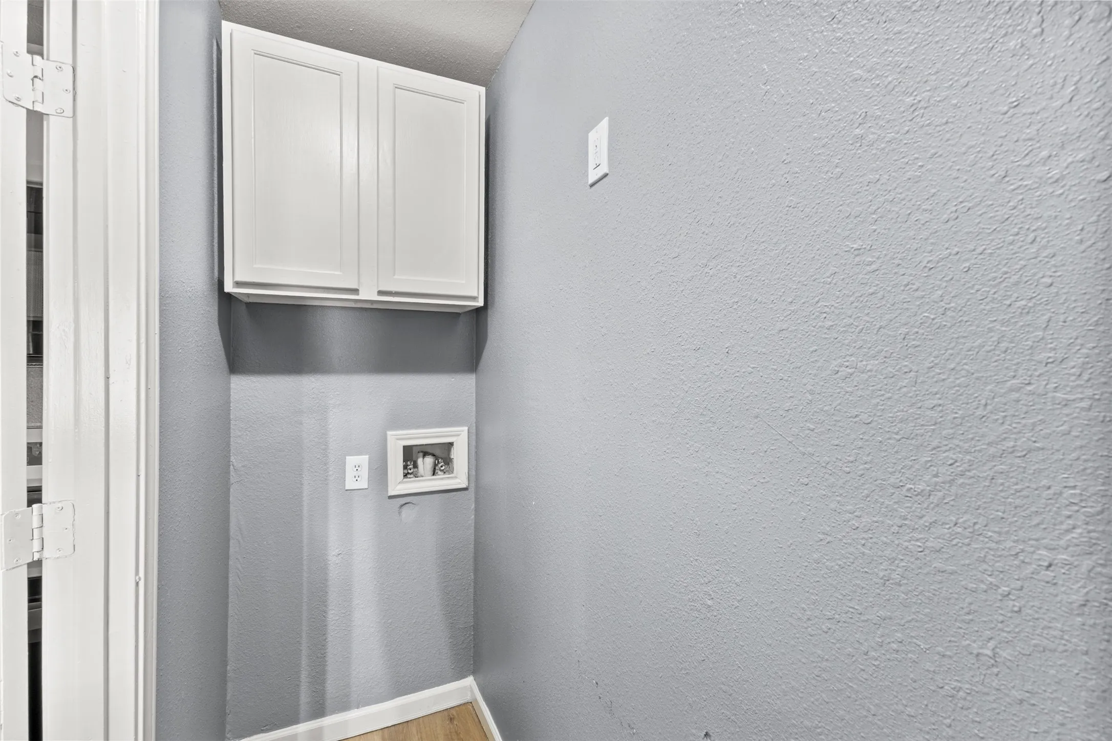 Laundry area featuring wood-finish flooring, white shaker-style cabinetry, and a utility hookup
