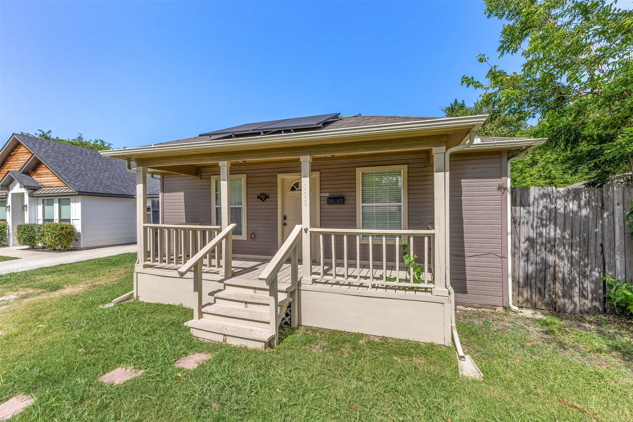 Exterior featuring a covered front porch with railings, a light-colored entry door, and solar panels on the roof