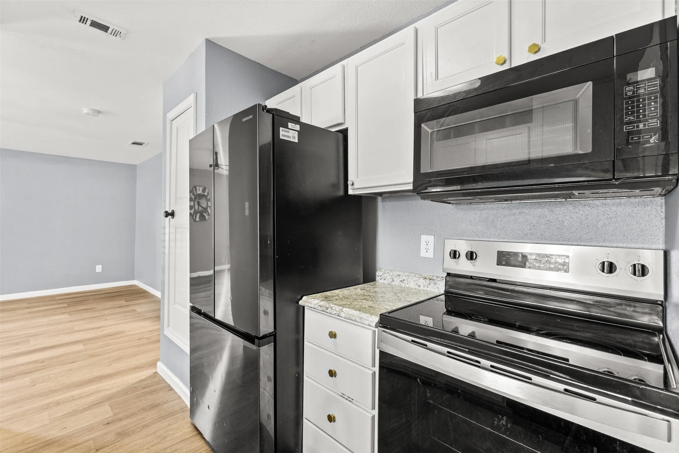 Kitchen featuring white cabinetry with gold-toned hardware, speckled countertops, and wood-finish flooring