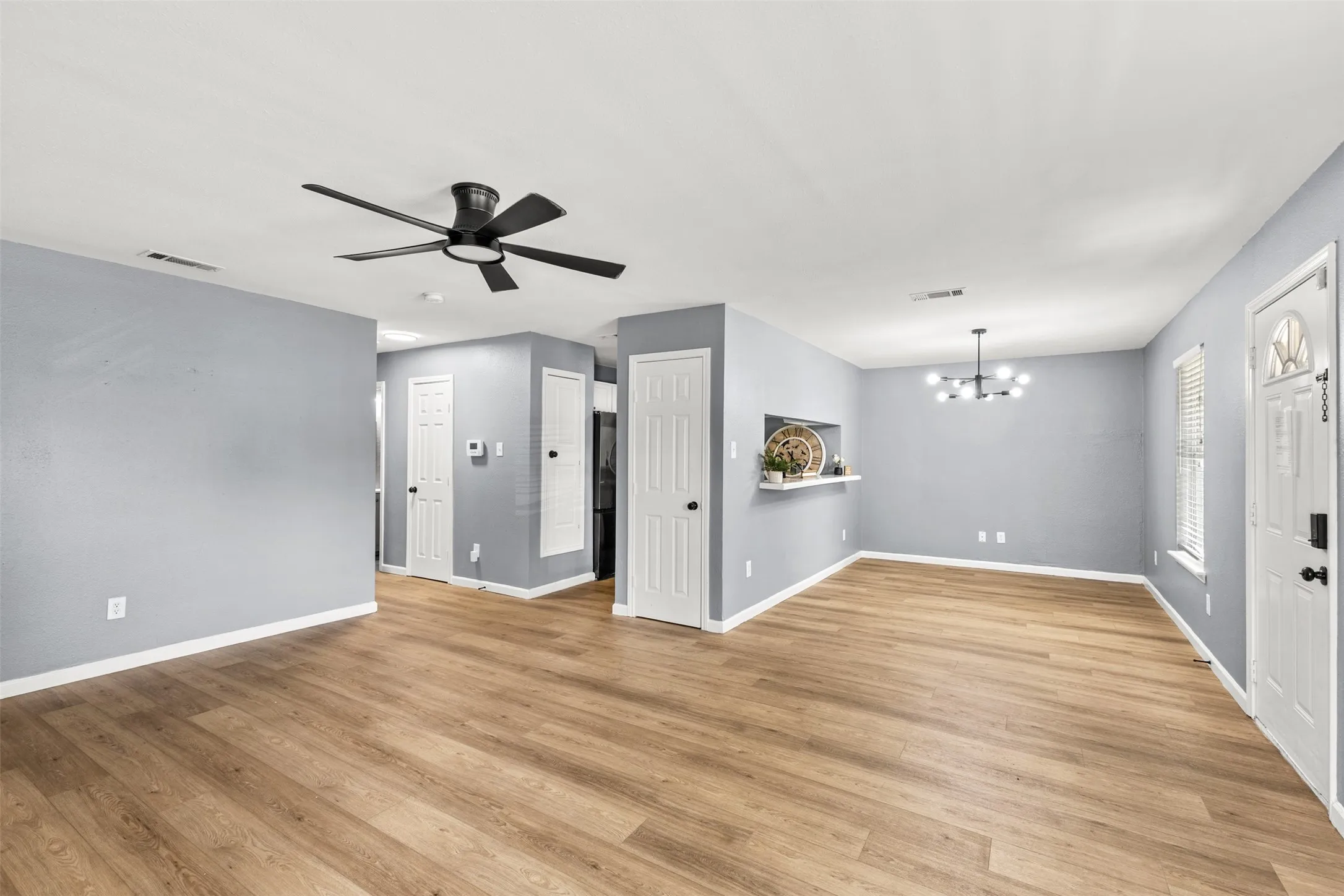 Spacious living area featuring wood-finish flooring, light gray walls, a modern ceiling fan, and a contemporary chandelier