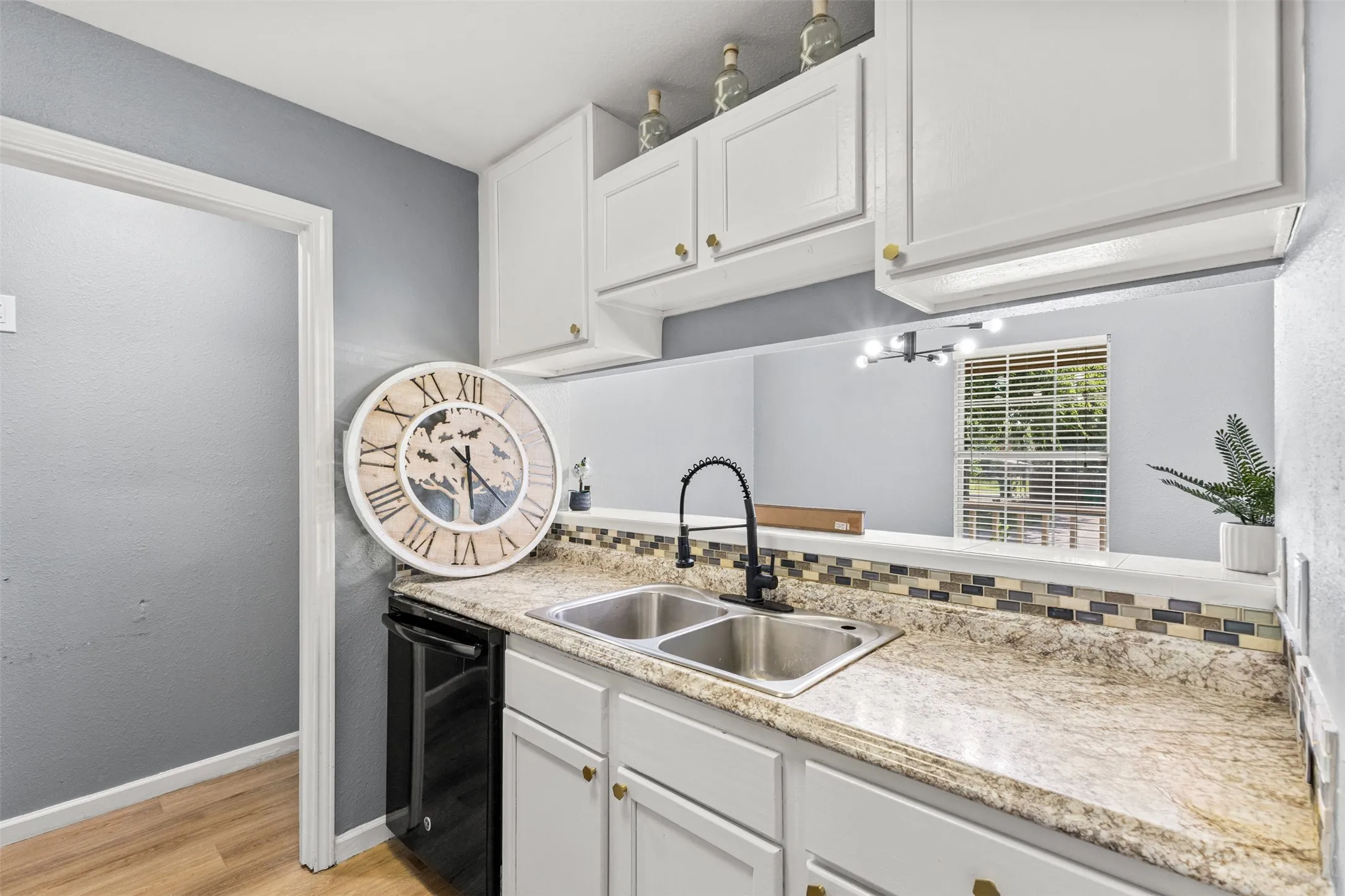 Kitchen featuring light-toned countertops, a double basin stainless steel sink with a matte black faucet, and a mosaic tile backsplash