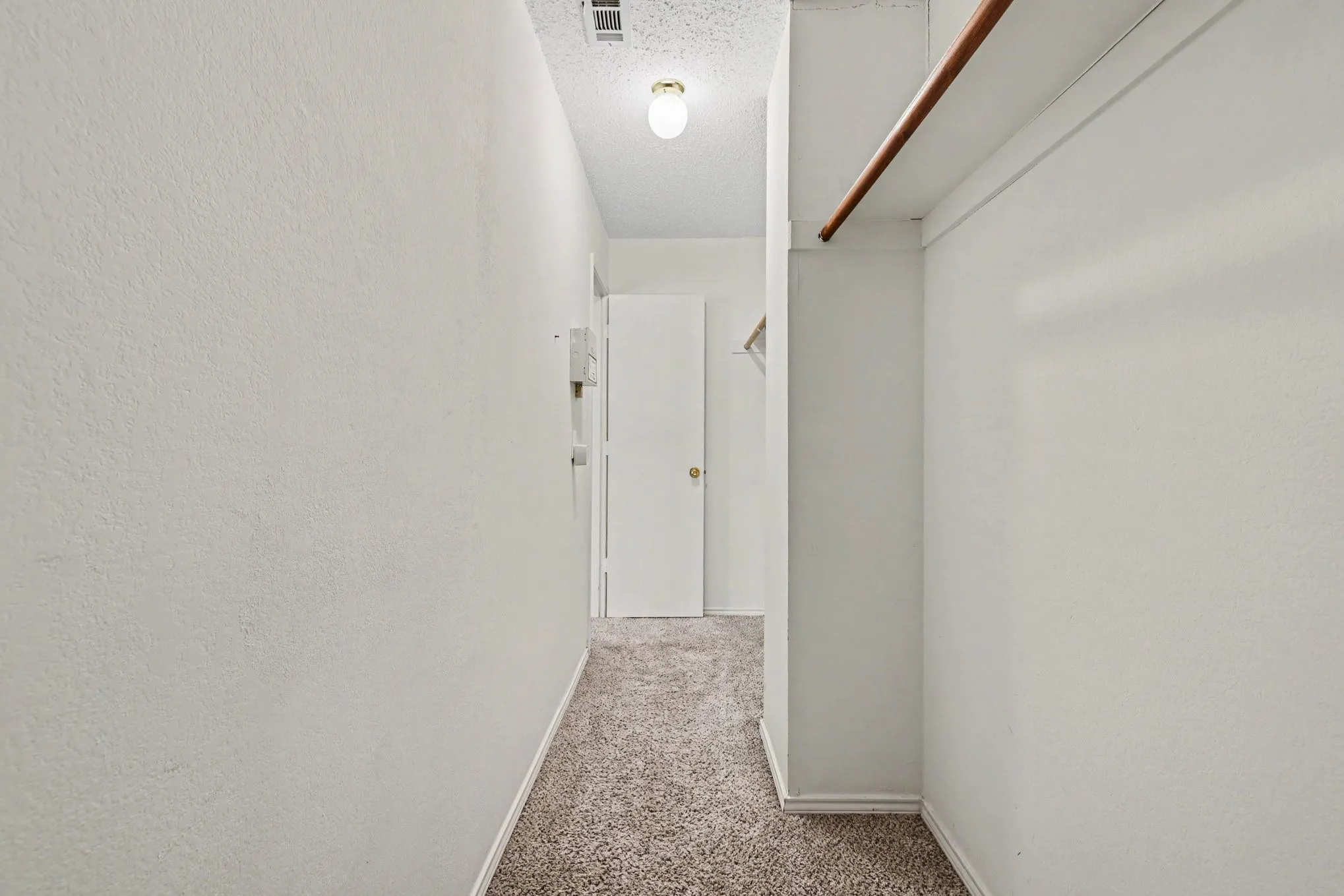 Walk-in closet with carpet flooring, a single wood hanging rod, and an upper shelf