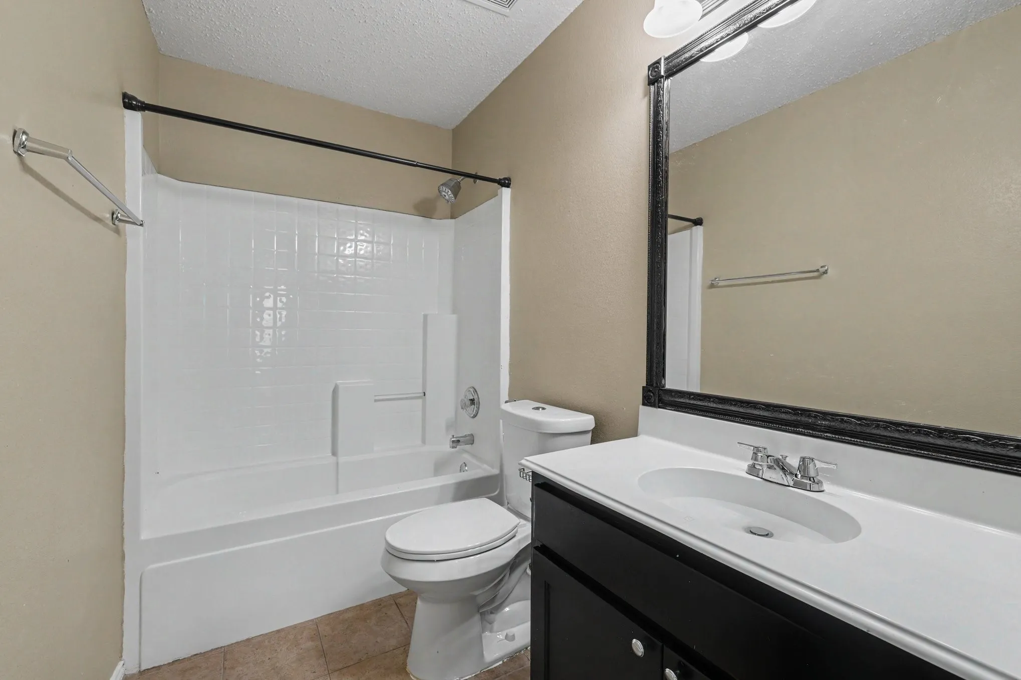 Bathroom featuring a white tub/shower combination with tile surround, a built-in vanity with a white countertop and integrated sink, a toilet, and a large wall-mounted mirror with a black frame