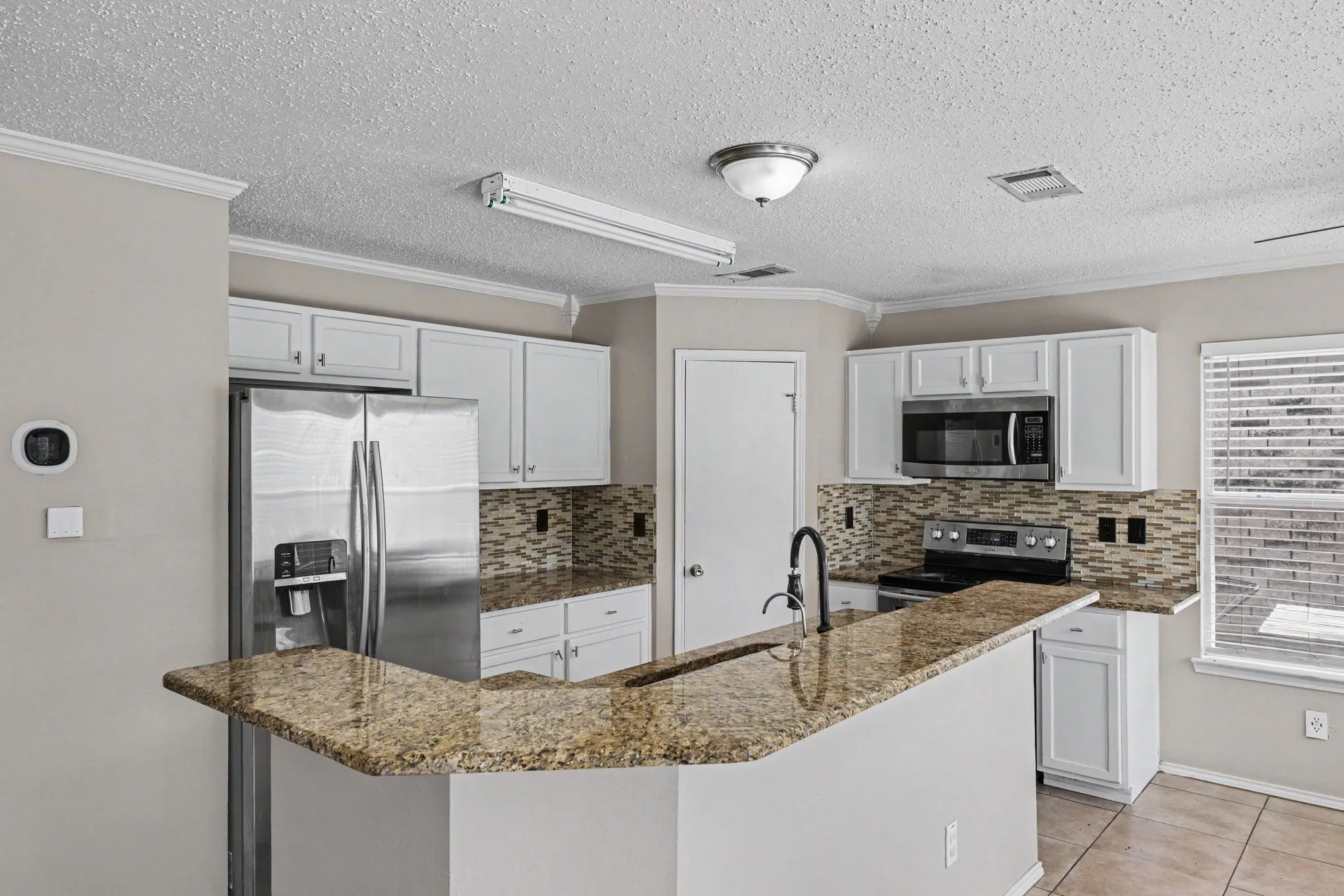 Kitchen featuring a breakfast bar with granite countertops, white cabinetry, and a tile backsplash
