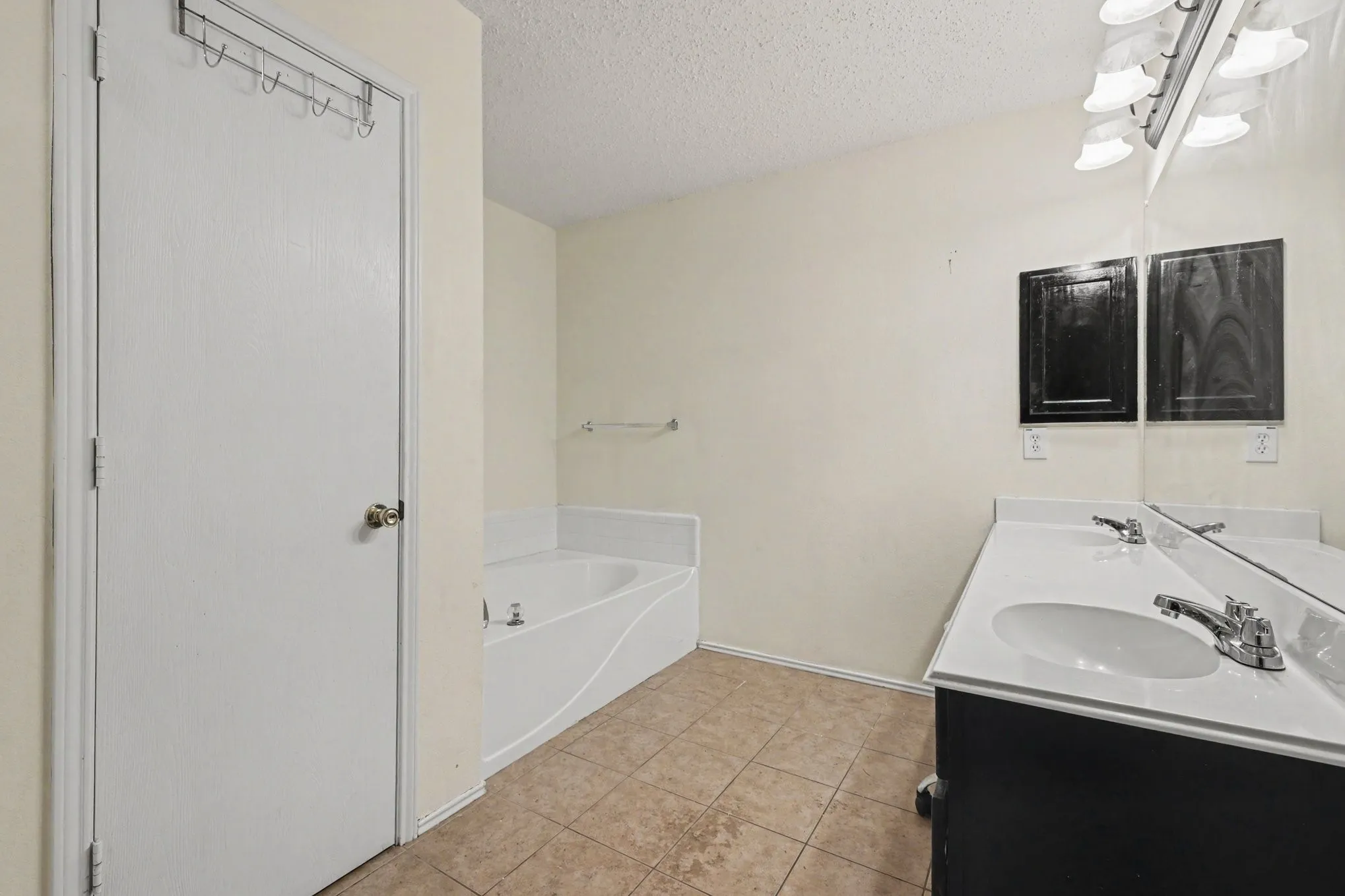 Bathroom featuring a dual-sink vanity with ample counter space, a large mirror, and a built-in garden tub