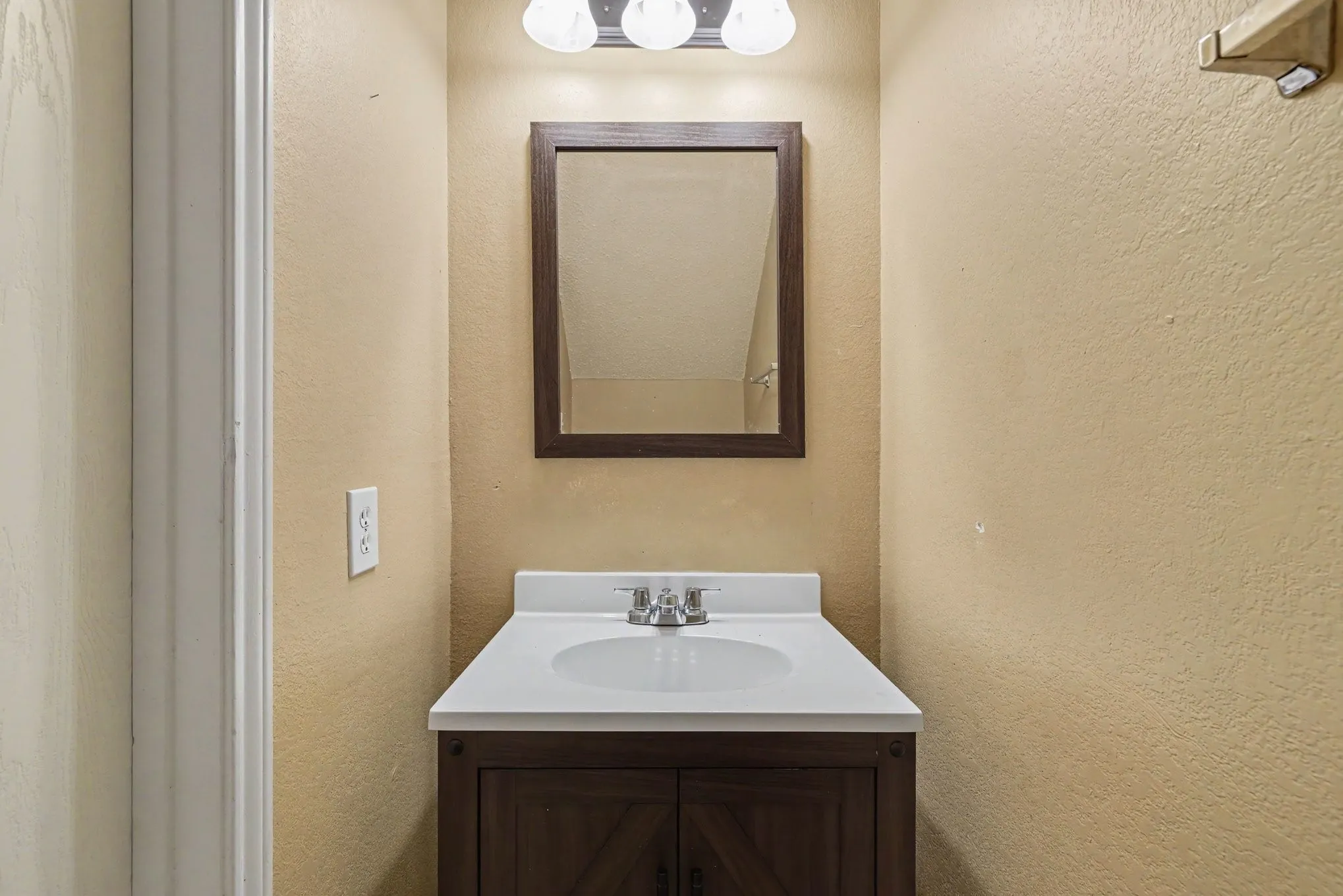 Bathroom vanity featuring a dark wood-finish cabinet, white countertop with integrated sink, chrome faucet, and rectangular mirror