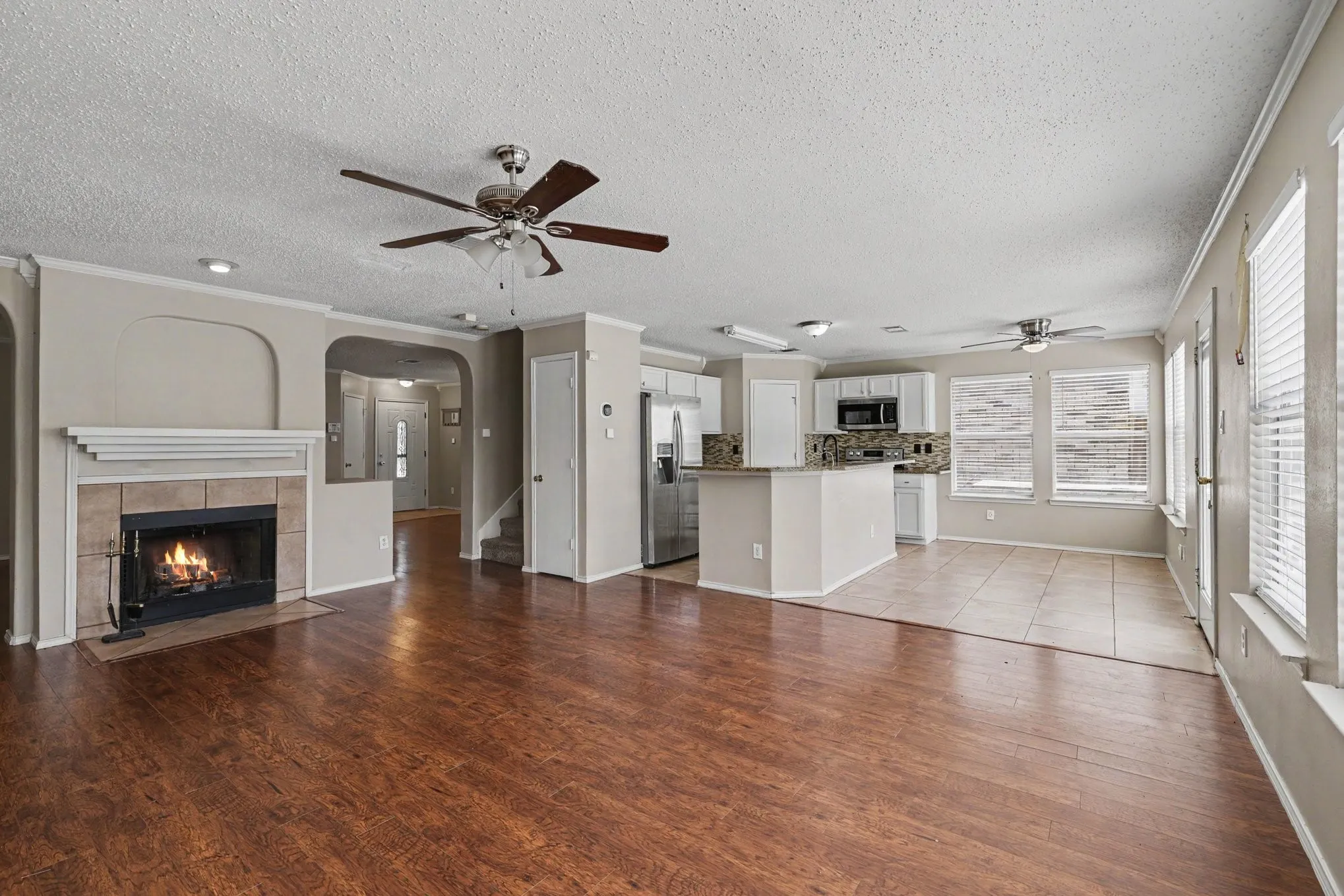 Spacious interior featuring wood-finish flooring, a tile-surround fireplace with mantel, and a kitchen with white cabinetry, stainless steel appliances, and a breakfast bar