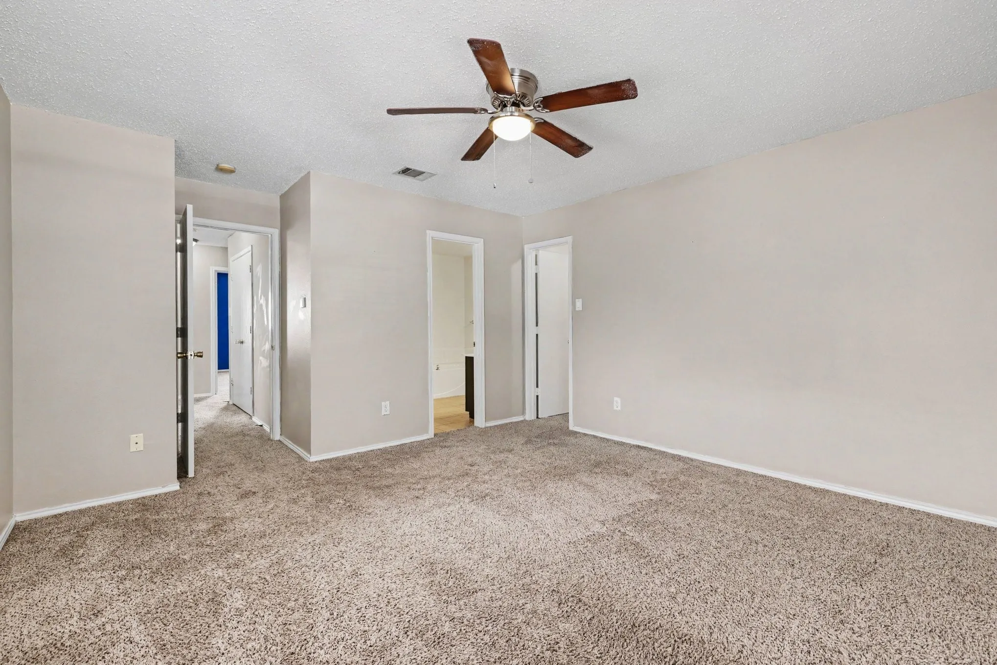 Spacious room featuring neutral-toned walls, textured carpeting, and a ceiling fan with integrated lighting