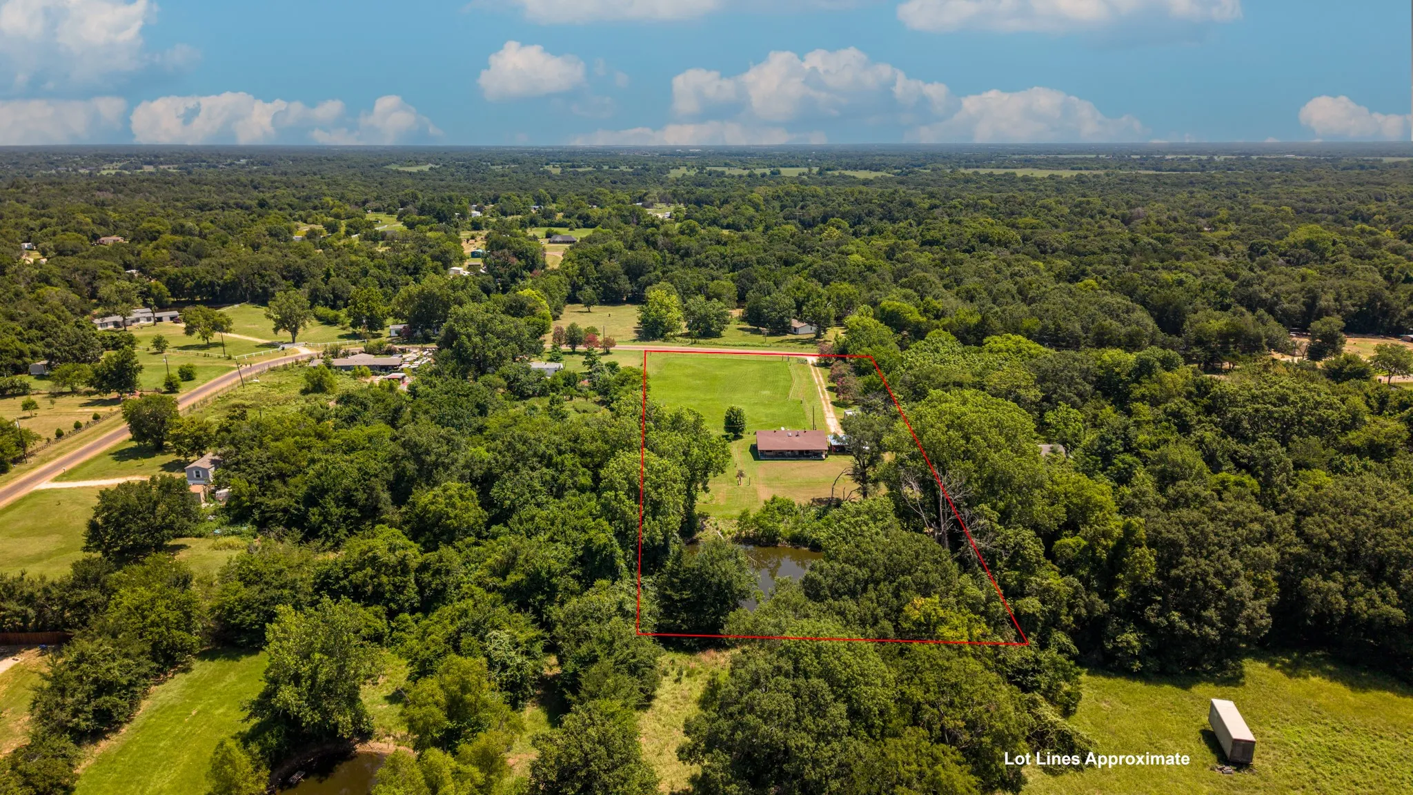 Expansive land parcel featuring a visible pond and a single-story residence