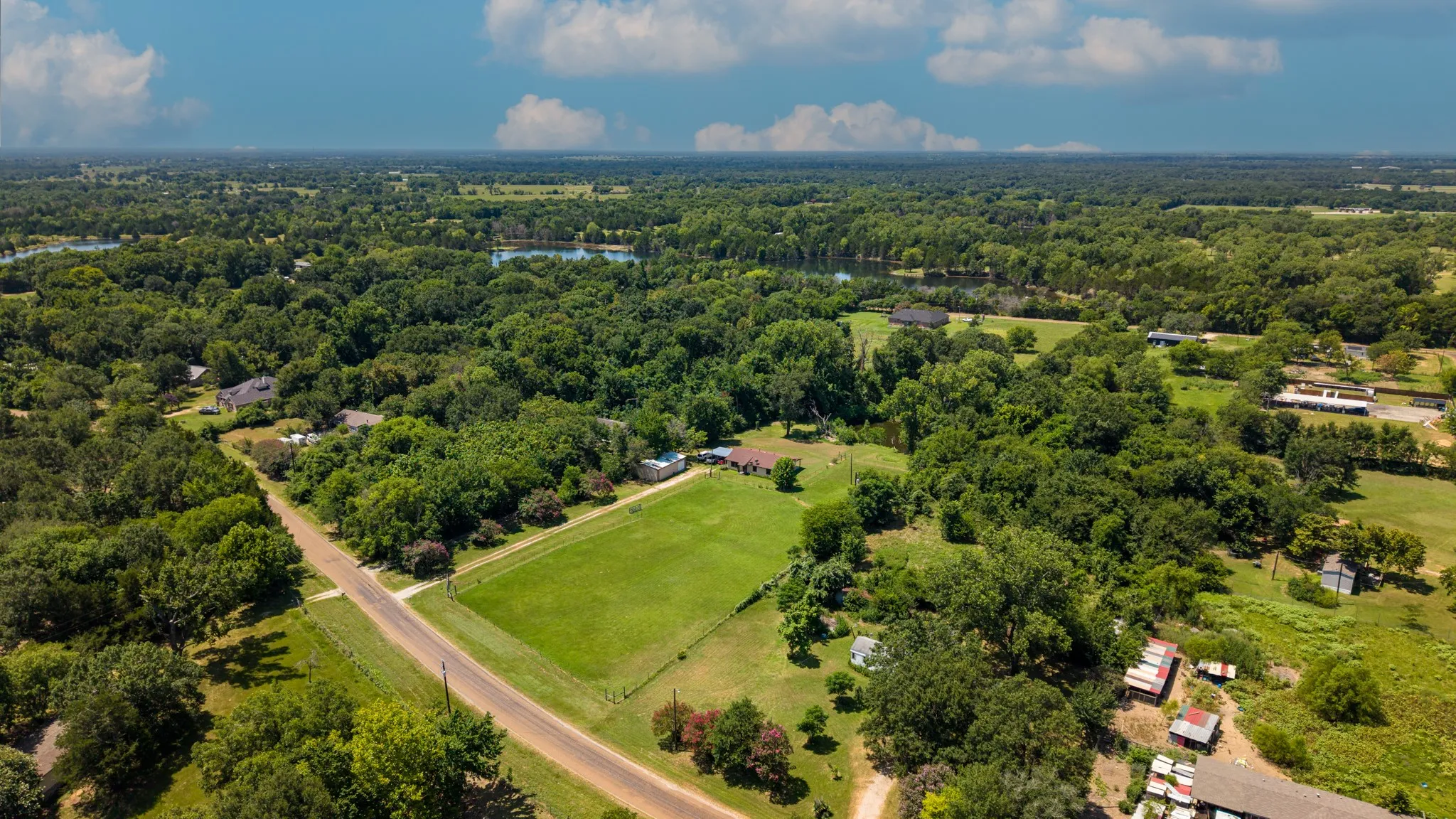Expansive rural landscape featuring a single-story residence, a large green field, and numerous mature trees