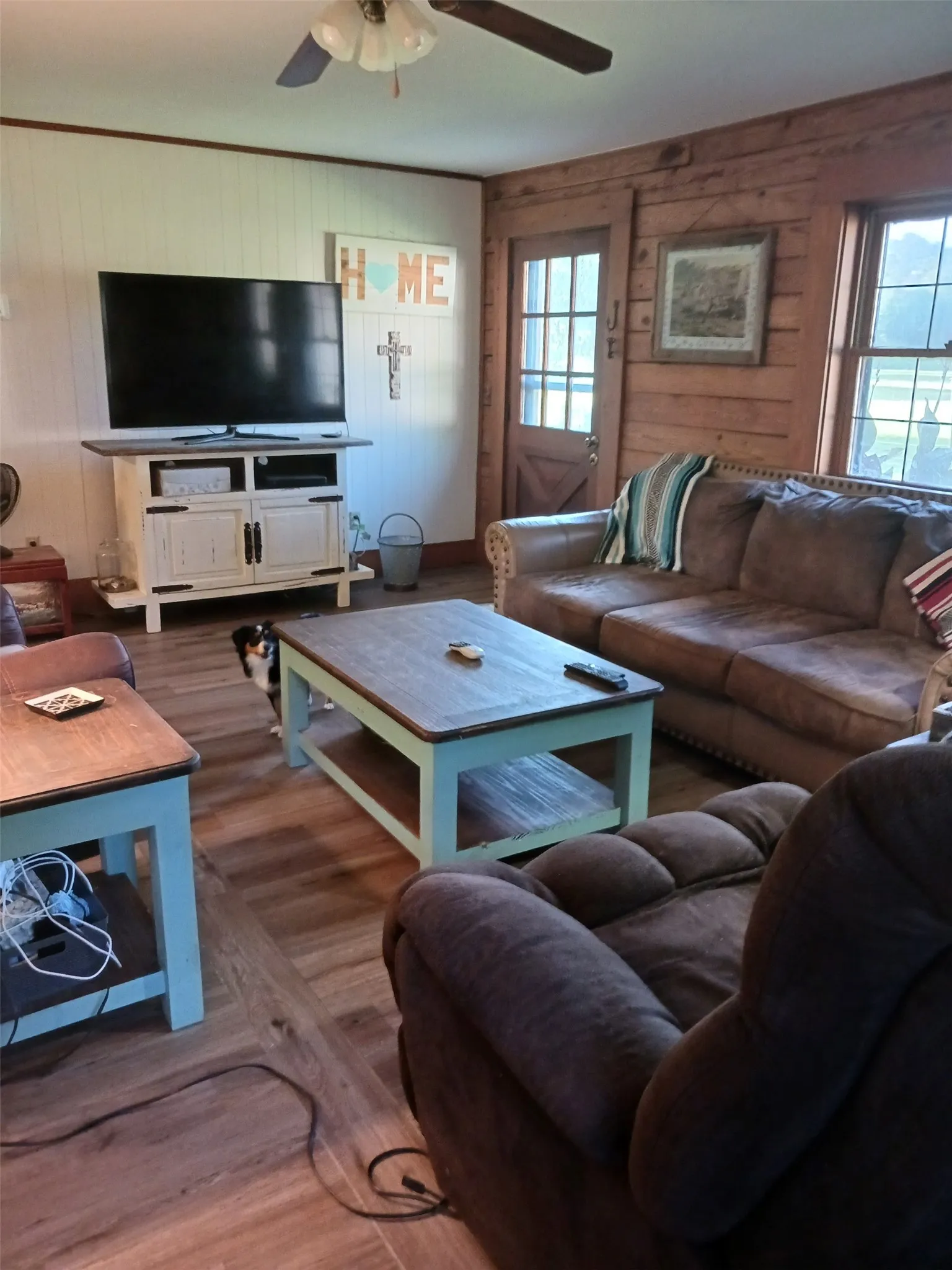 Open-concept living space featuring wood-finish flooring, plank wood walls, and a ceiling fan