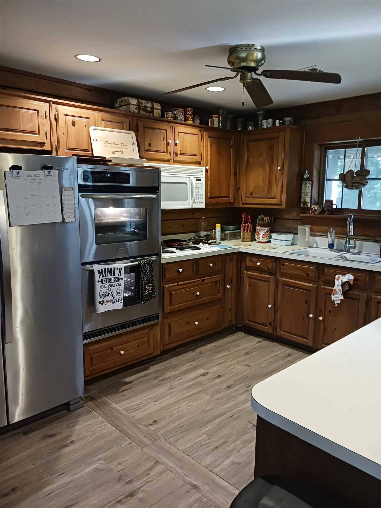 Open-concept living area featuring a kitchen with wood cabinetry, light-toned countertops, and wood-finish flooring