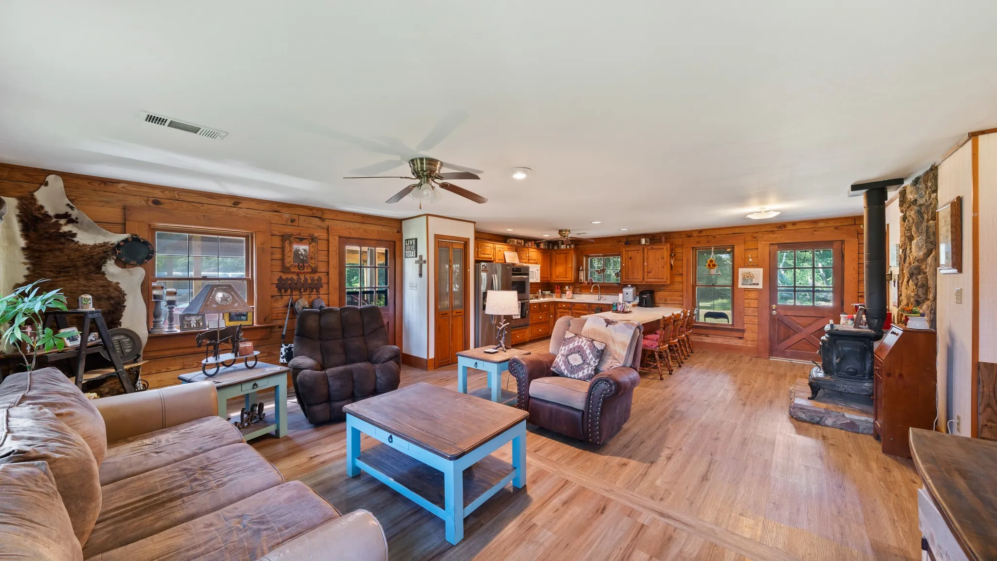 Open-concept living space featuring wood-finish flooring, plank wood walls, and a ceiling fan