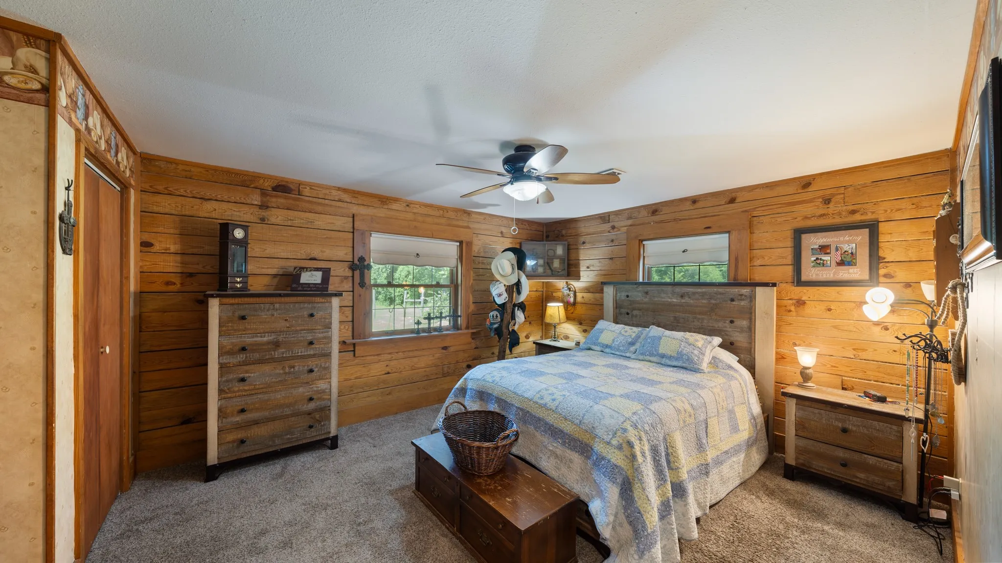 Wood-paneled room featuring a ceiling fan with integrated lighting, twin windows with exterior views, and a solid wood door