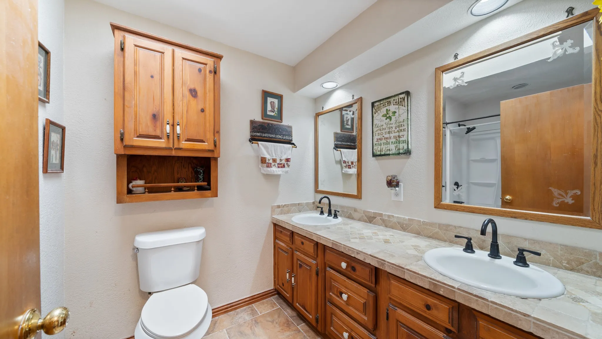 Bathroom featuring a double vanity with integrated sinks, tile countertop, and wood cabinetry