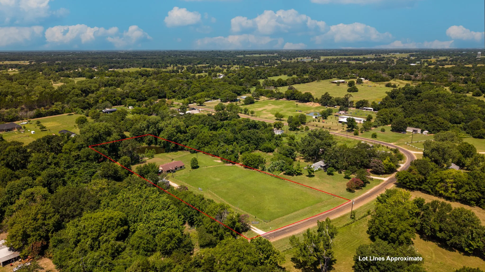 Expansive acreage featuring a single-story residence with a brown shingle roof, surrounded by mature trees and open green spaces