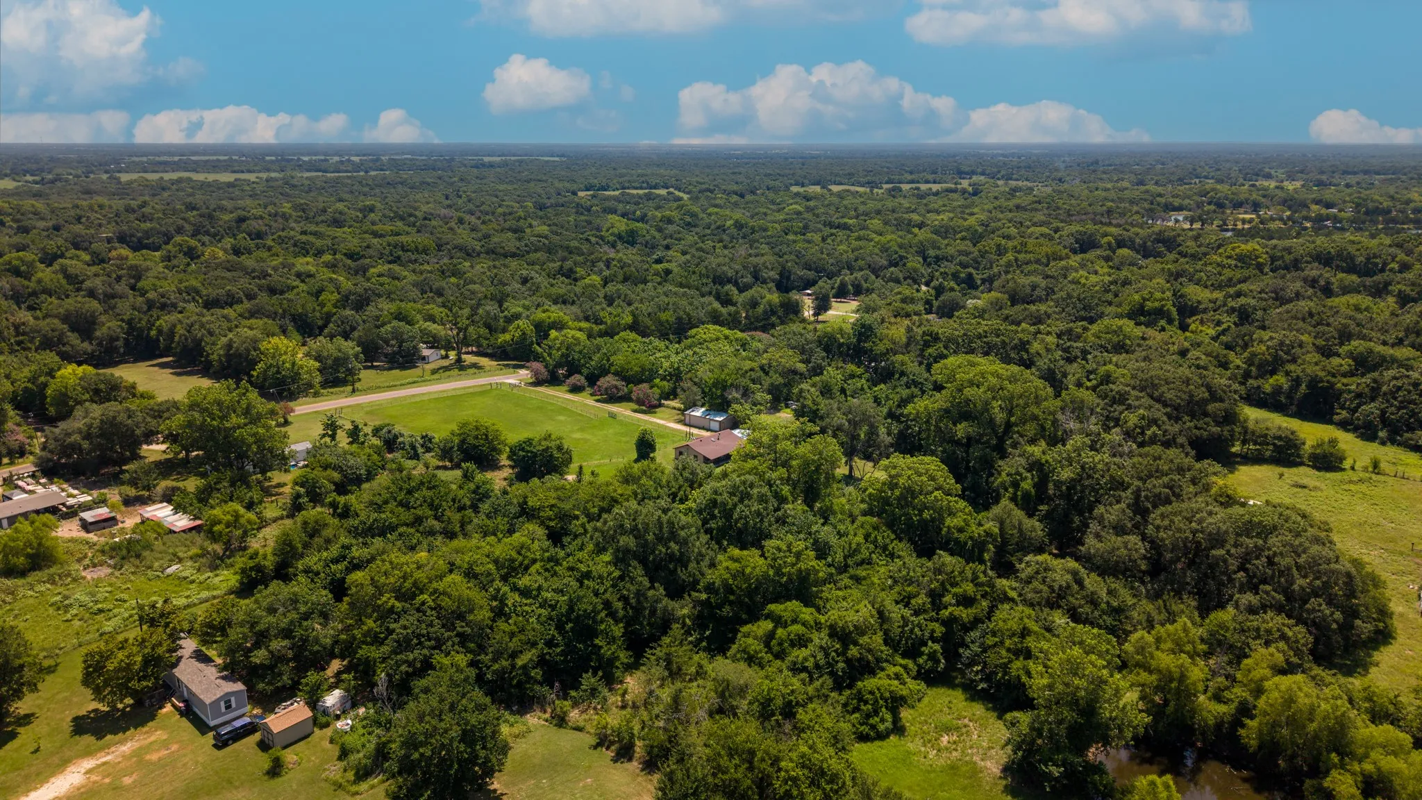 Expansive wooded property featuring a cleared central area, several structures, and abundant mature trees