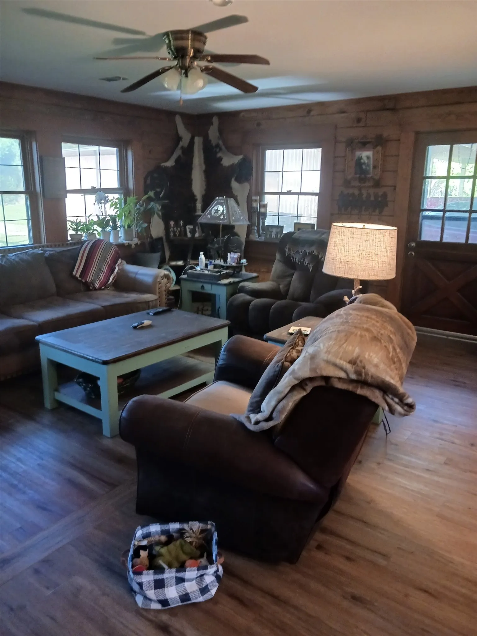 Open-concept living space featuring wood-finish flooring, wood plank walls, and multiple windows for natural light