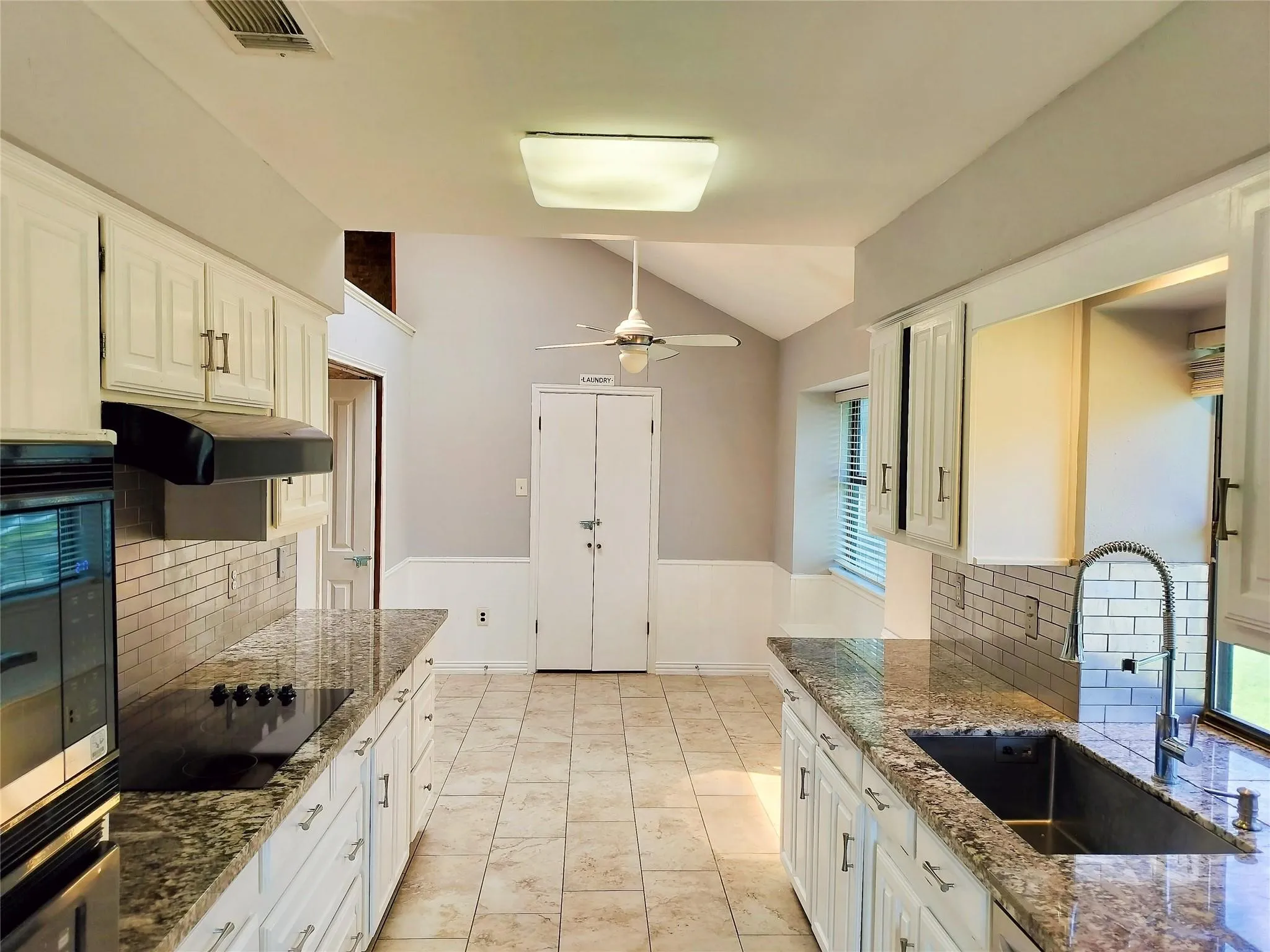 Galley-style kitchen featuring light-toned cabinetry with brass-finish hardware, speckled countertops, and a subway tile backsplash