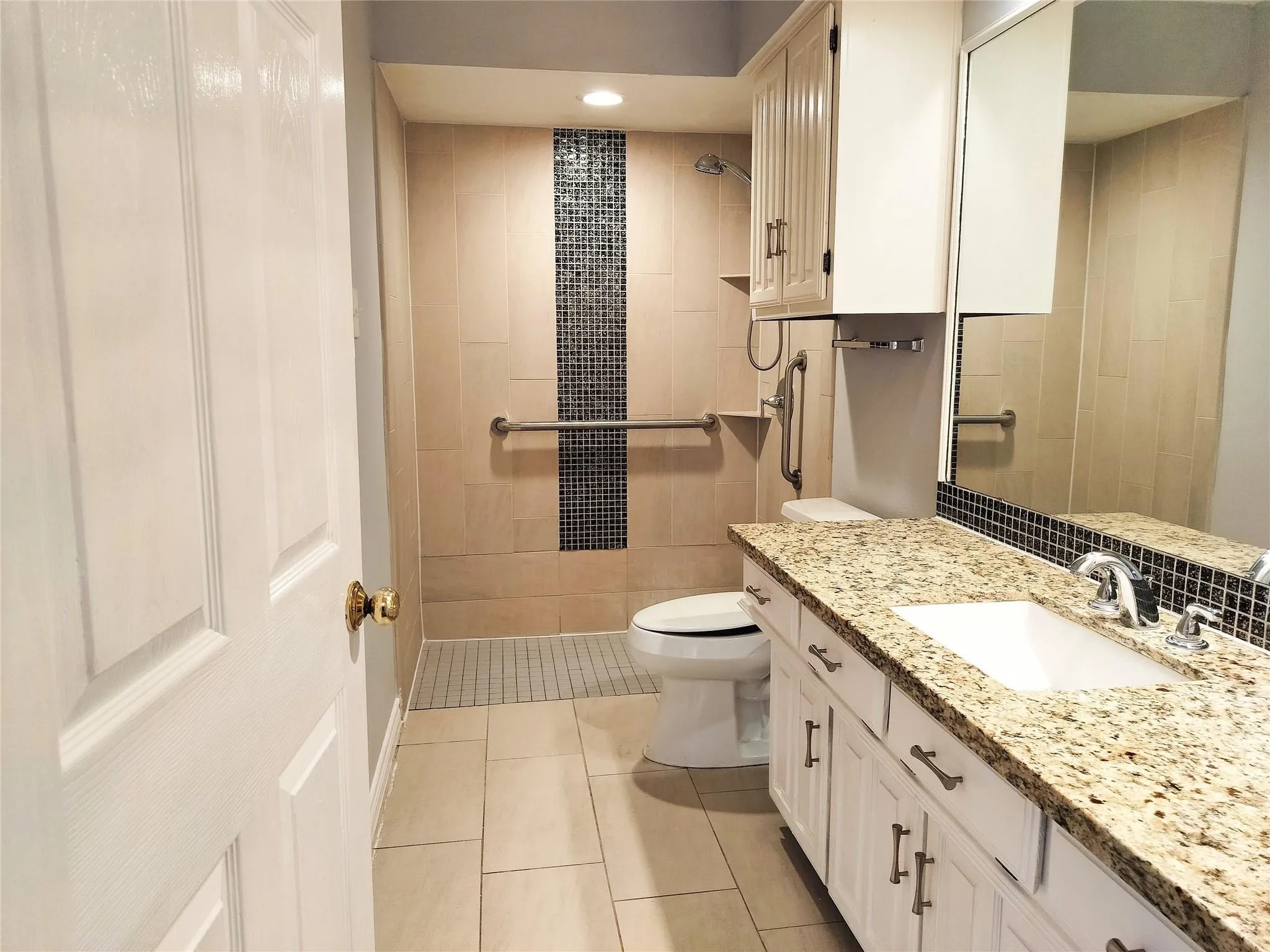 Bathroom vanity featuring a light-toned stone countertop, integrated sink, and white cabinetry with dark hardware