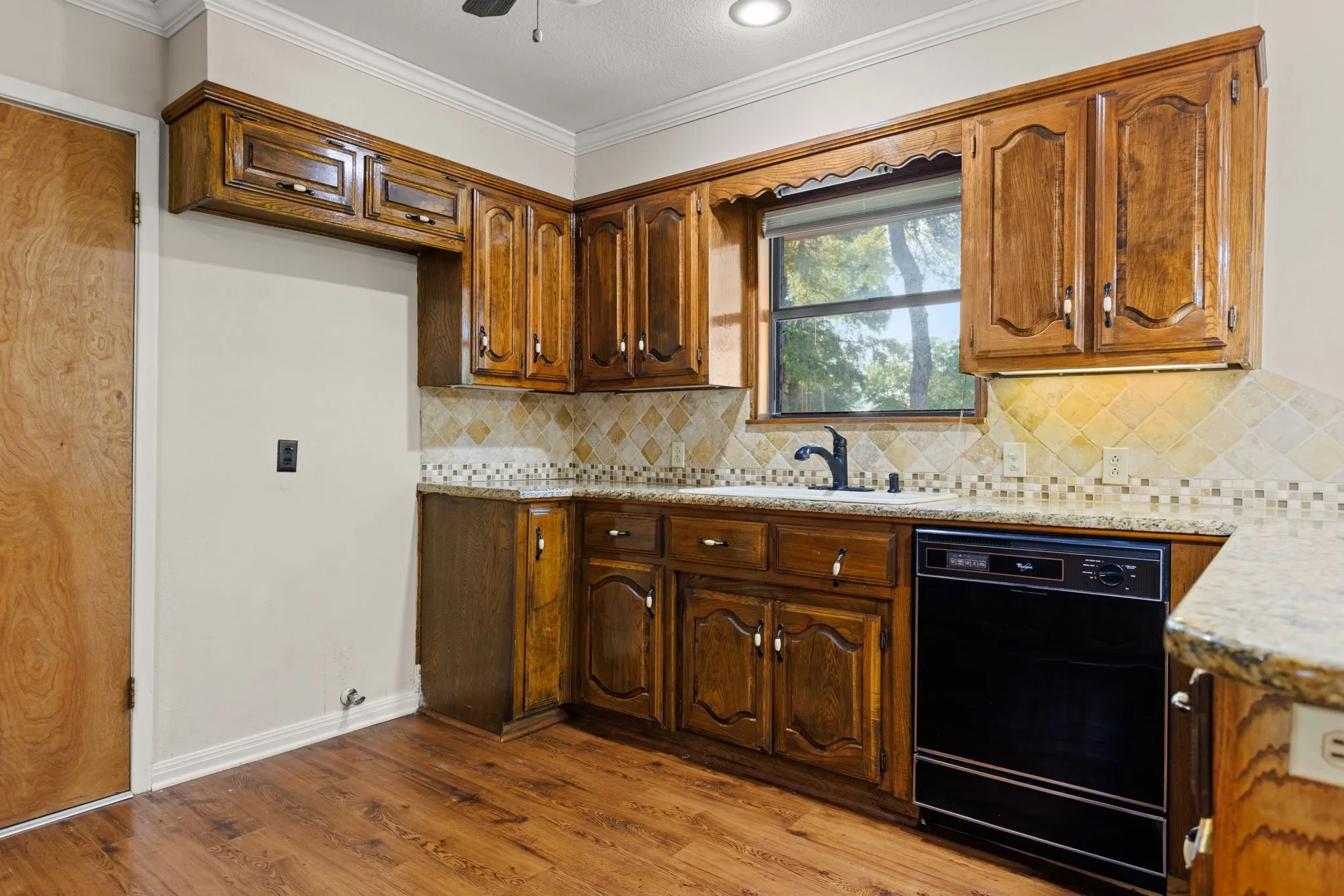 Kitchen featuring wood-finish flooring, wood cabinetry with decorative hardware, granite-look countertops, and a tile backsplash