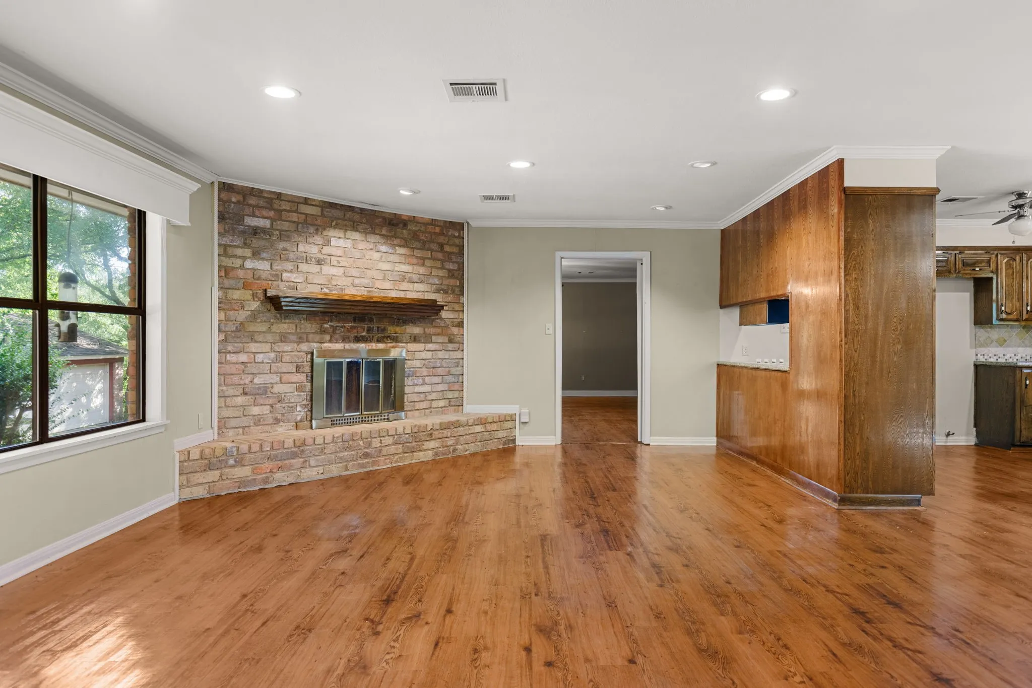Expansive living space featuring wood-finish flooring, a brick-faced fireplace with a hearth and mantel, recessed lighting, and a large window