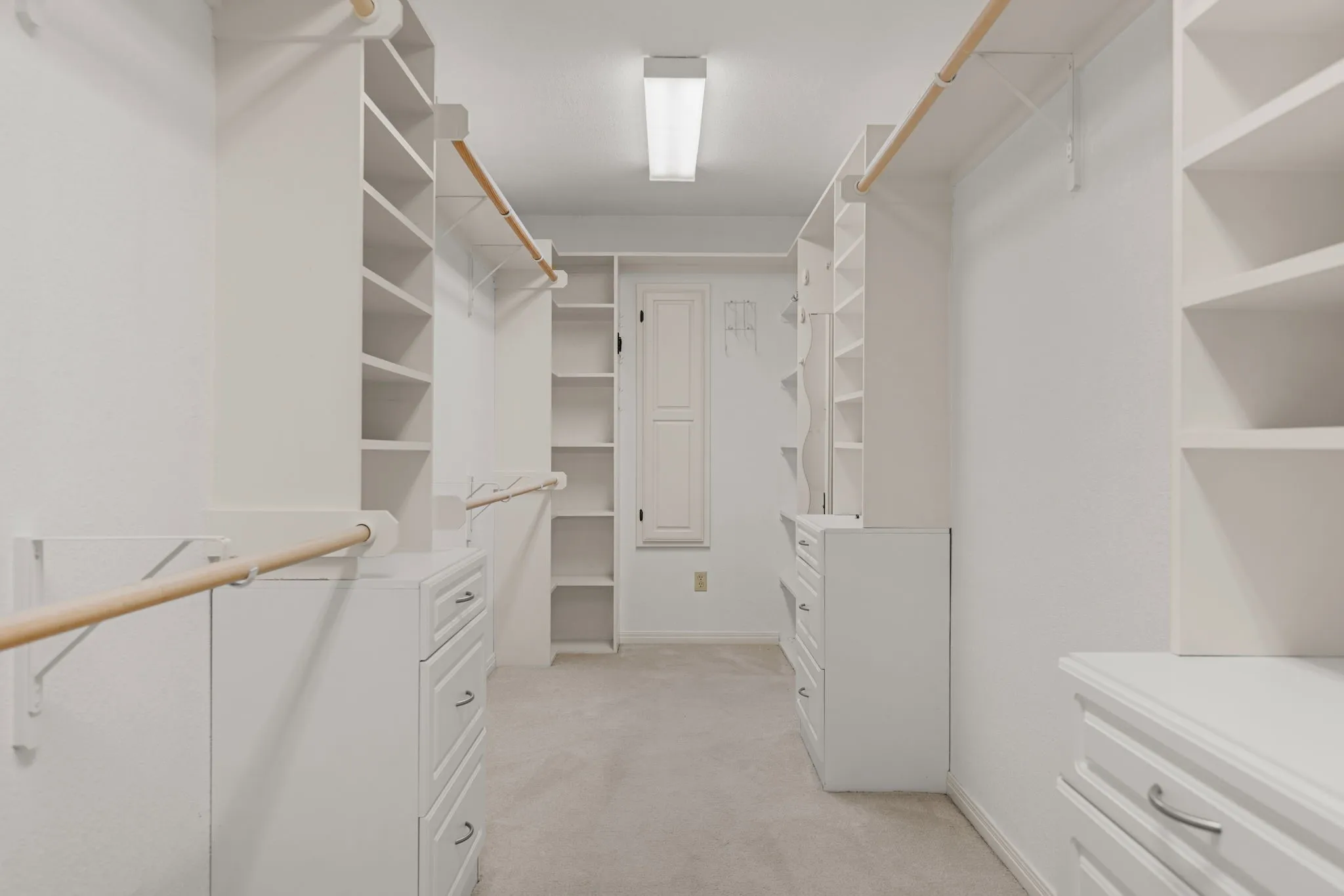 Spacious walk-in closet featuring extensive built-in shelving, multiple hanging rods, integrated drawer units, and neutral carpeting