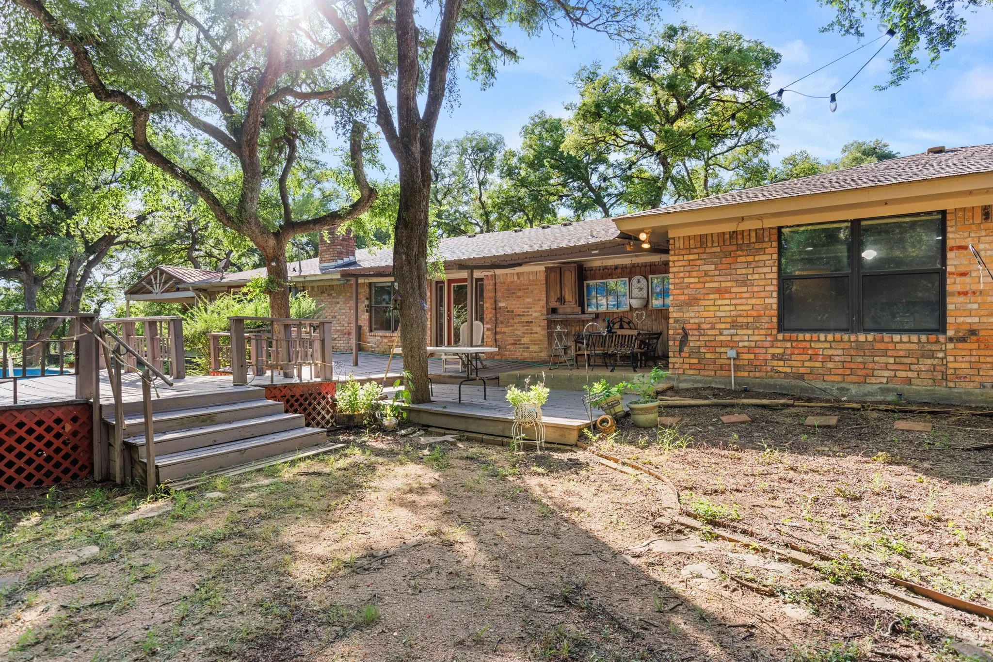 Expansive backyard featuring a multi-level wood deck with lattice skirting, mature trees, and a brick exterior home with a covered patio area
