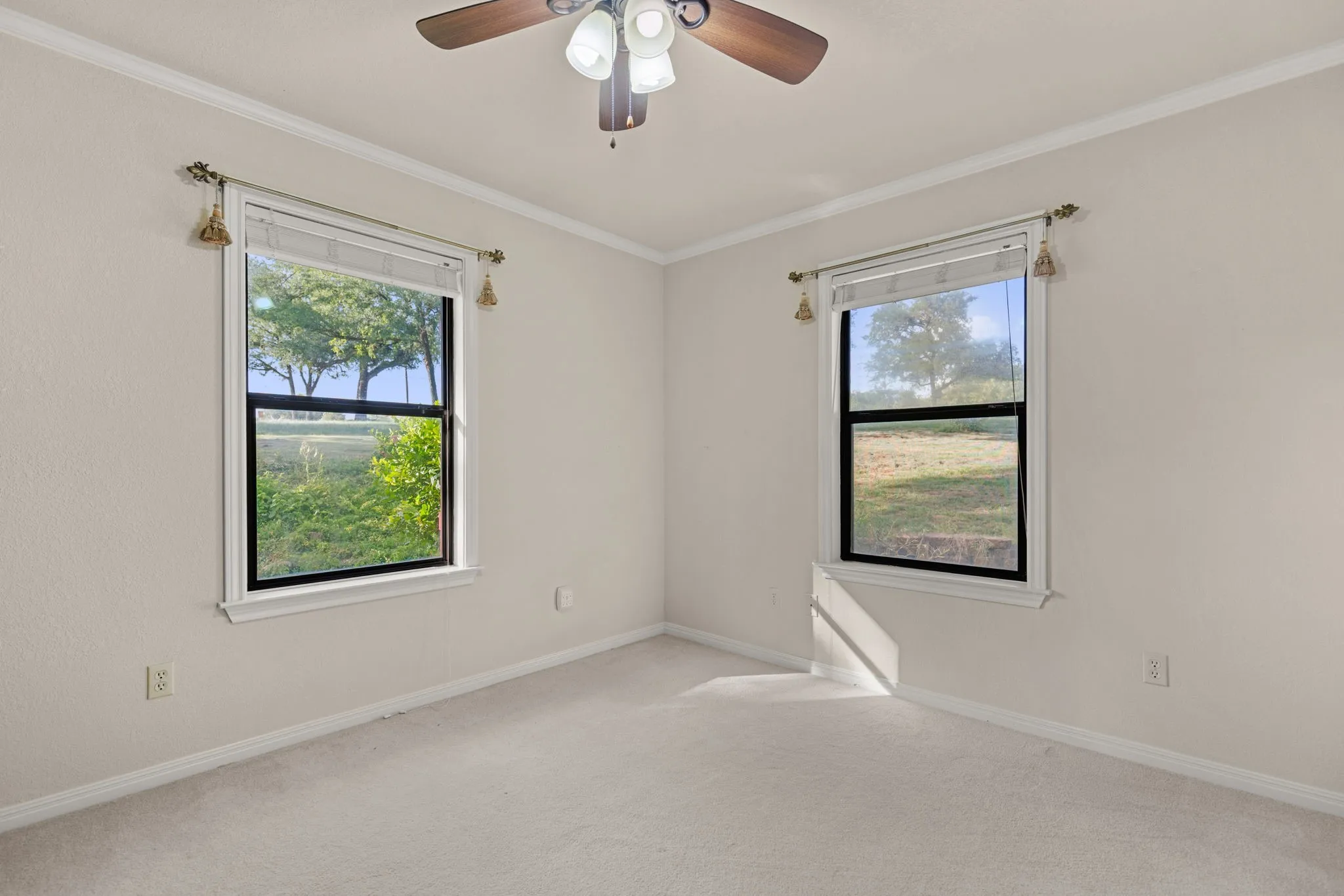 Neutral tone walls with crown molding, two windows with black frames, and a ceiling fan with integrated lighting