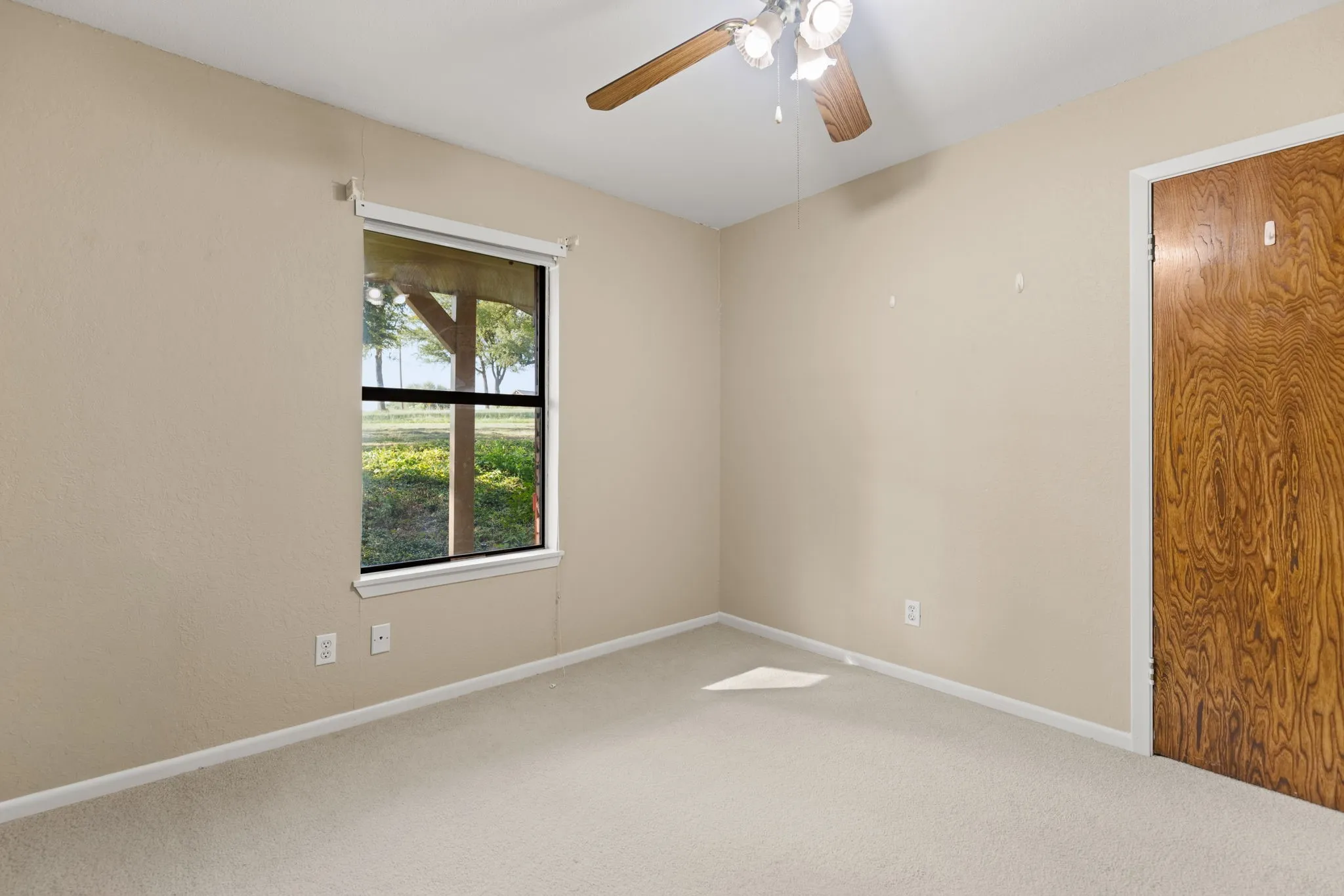 Carpeted room with a ceiling fan, a window, and a wood-finish door