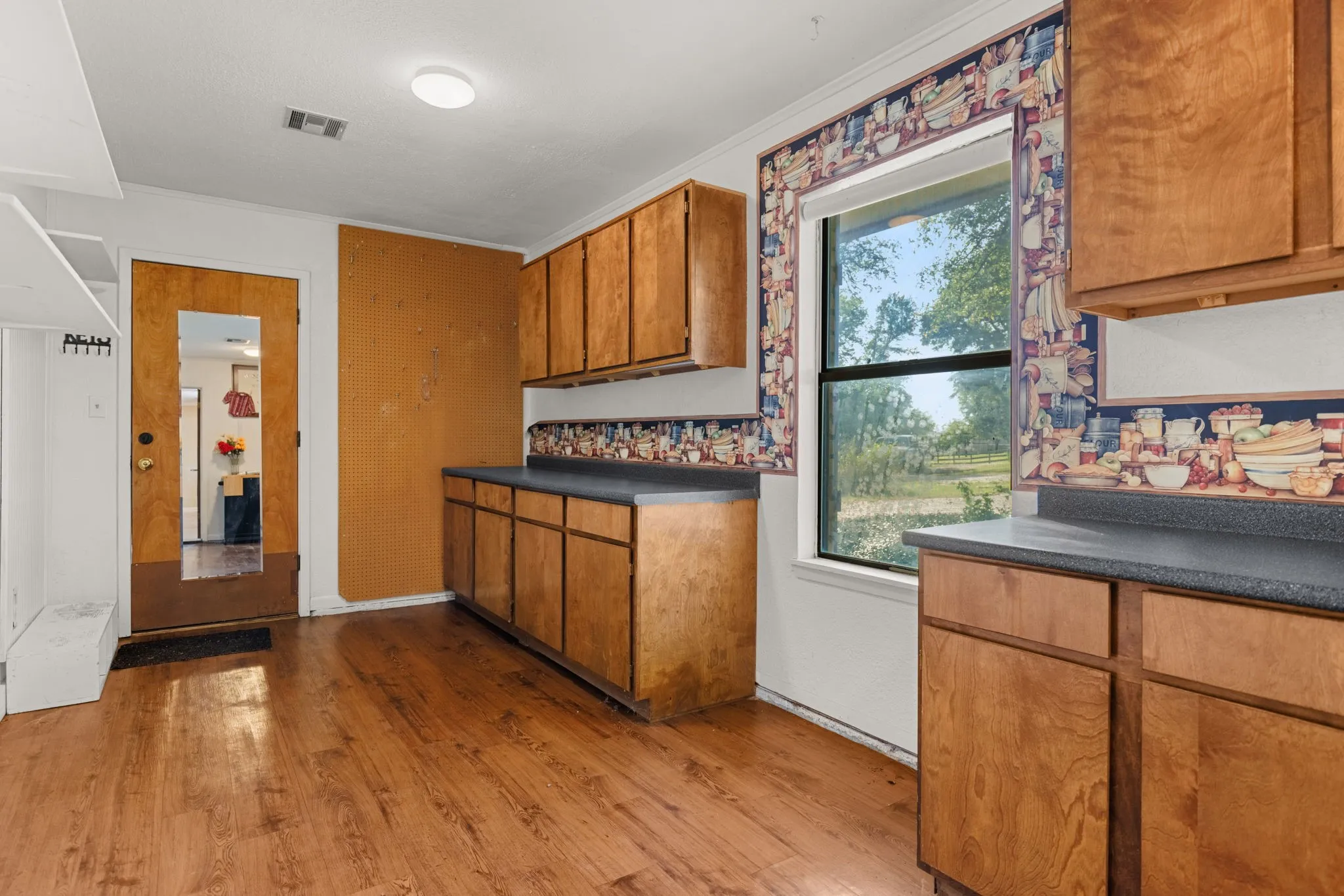 Wood-finish flooring throughout, featuring extensive cabinetry with dark countertops, and a full-light door with a coat rack