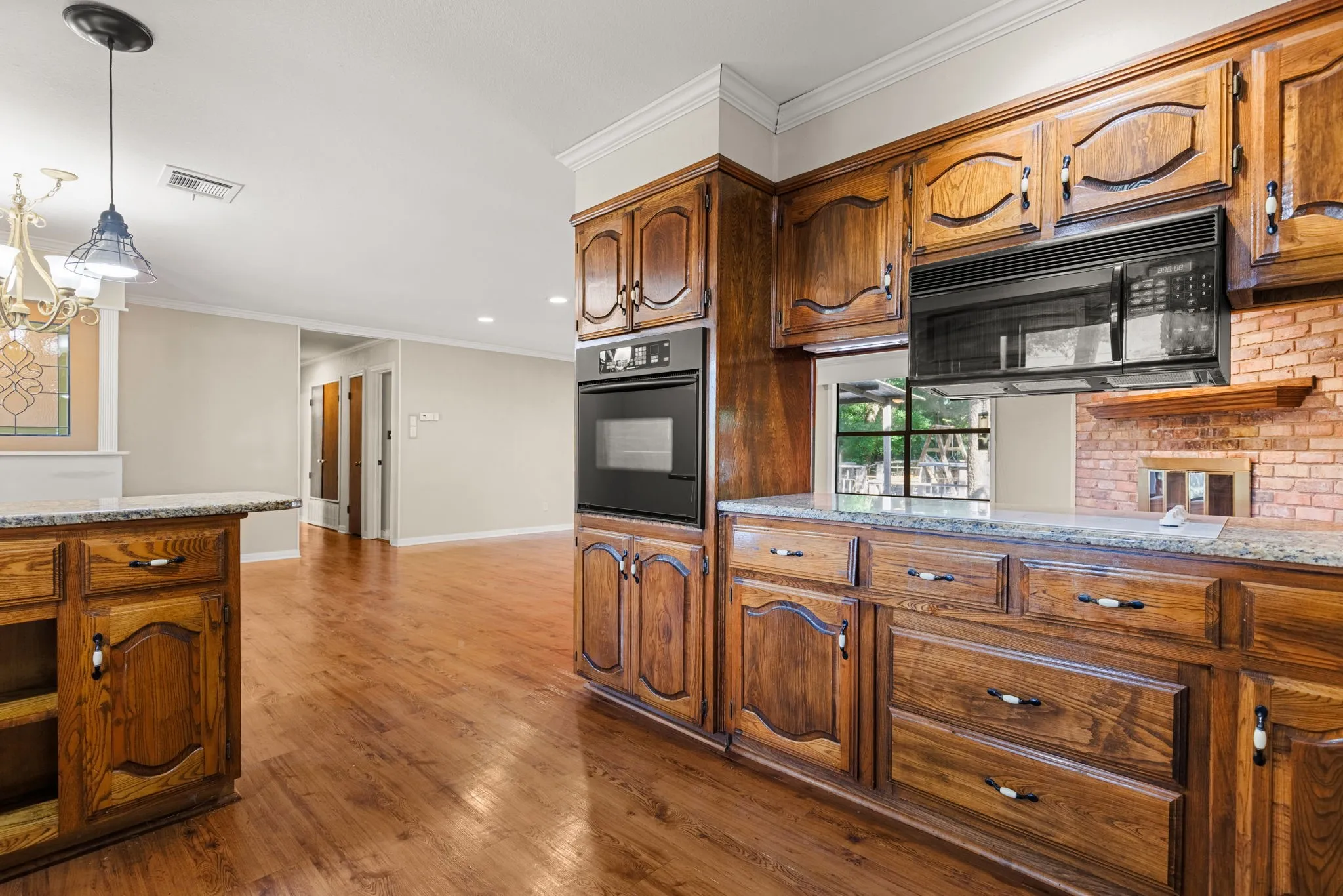 Kitchen featuring rich wood cabinetry, stone countertops, built-in oven, microwave, and wood-finish flooring