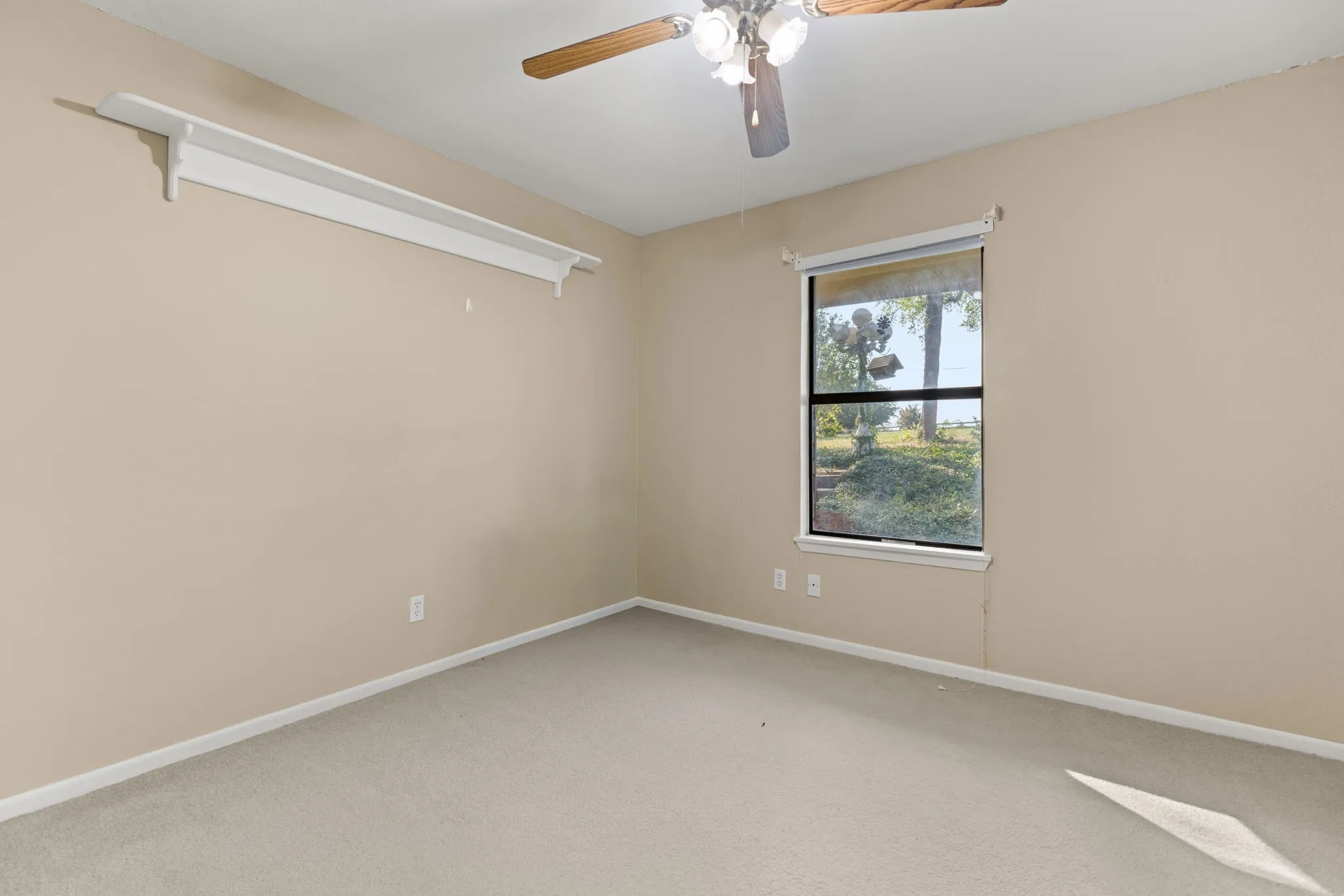Carpeted room featuring a single window with outdoor scenery, neutral wall paint, white baseboards, and a ceiling fan with light fixture