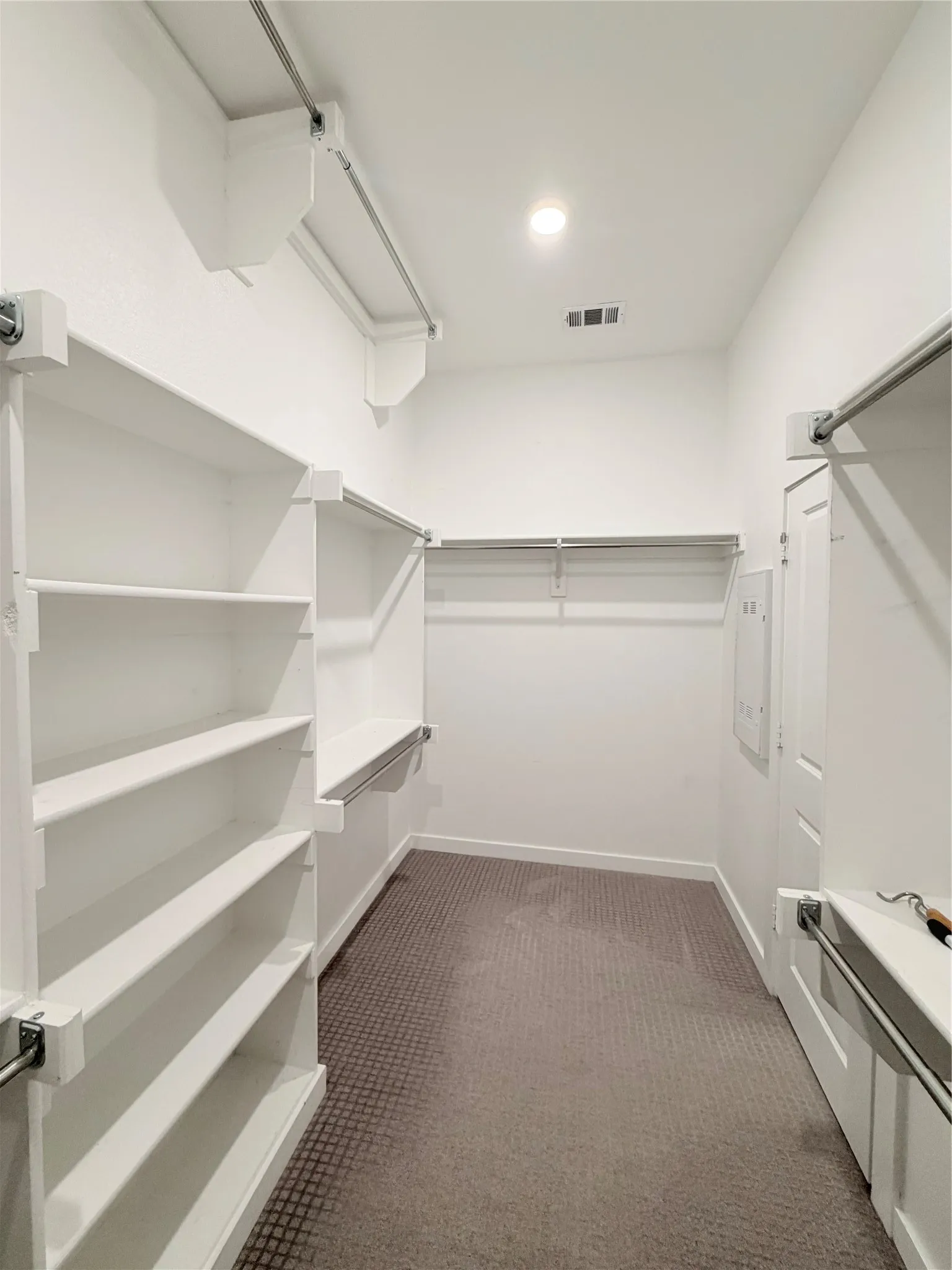 Walk-in closet featuring built-in shelving, multiple hanging rods, recessed ceiling lighting, and patterned carpet flooring