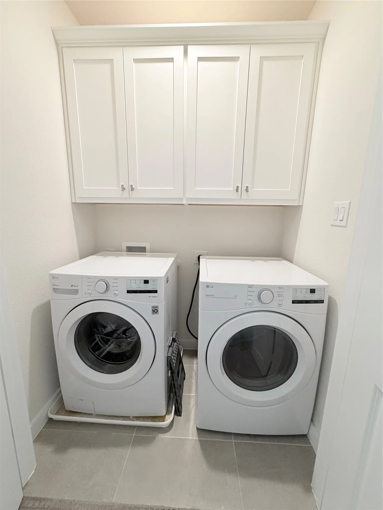 Dedicated laundry area featuring overhead white shaker cabinetry, light gray tile flooring, and white walls