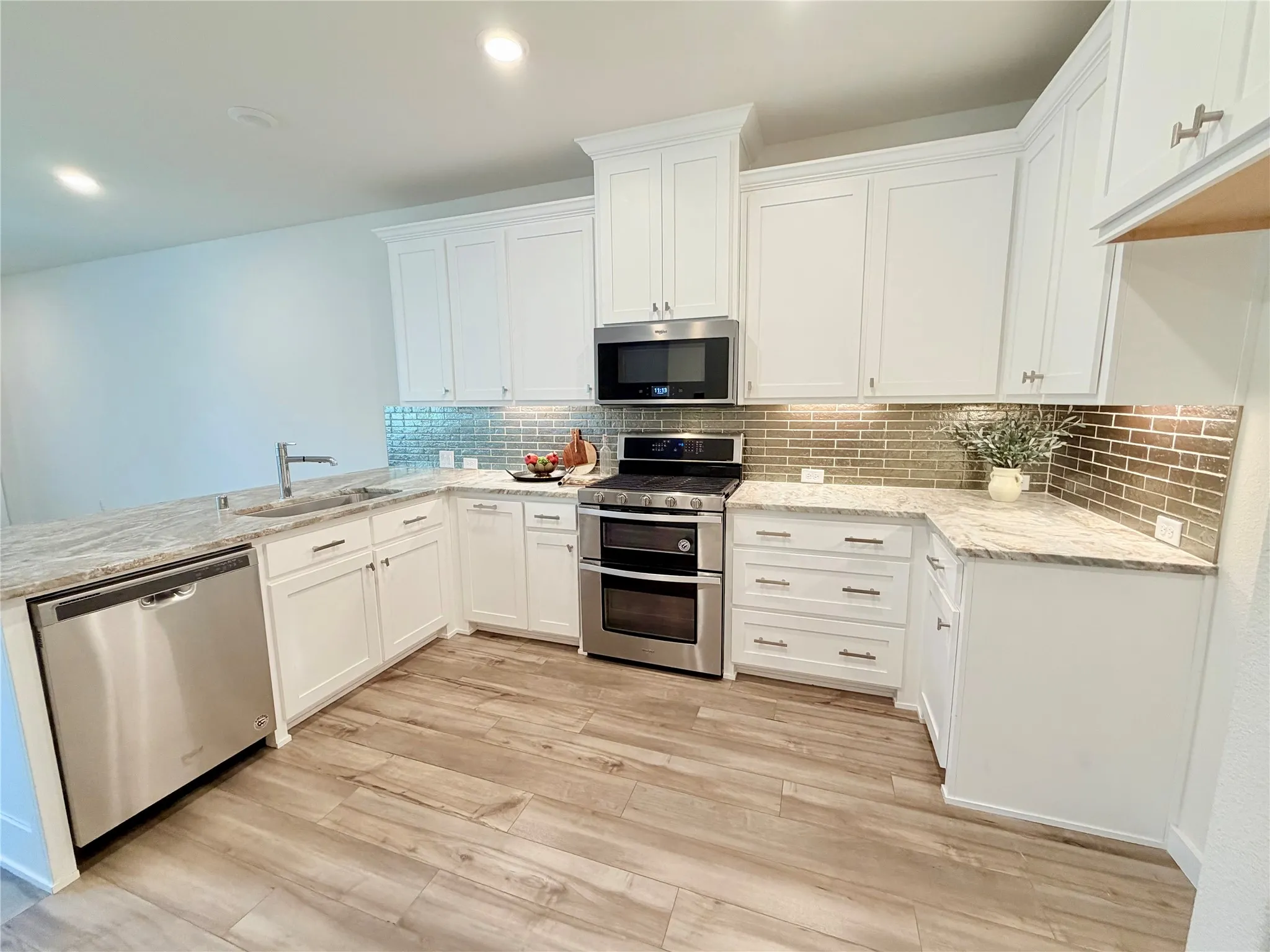 Contemporary kitchen featuring white cabinetry, stone countertops, a subway tile backsplash, stainless steel appliances, and wood-finish flooring
