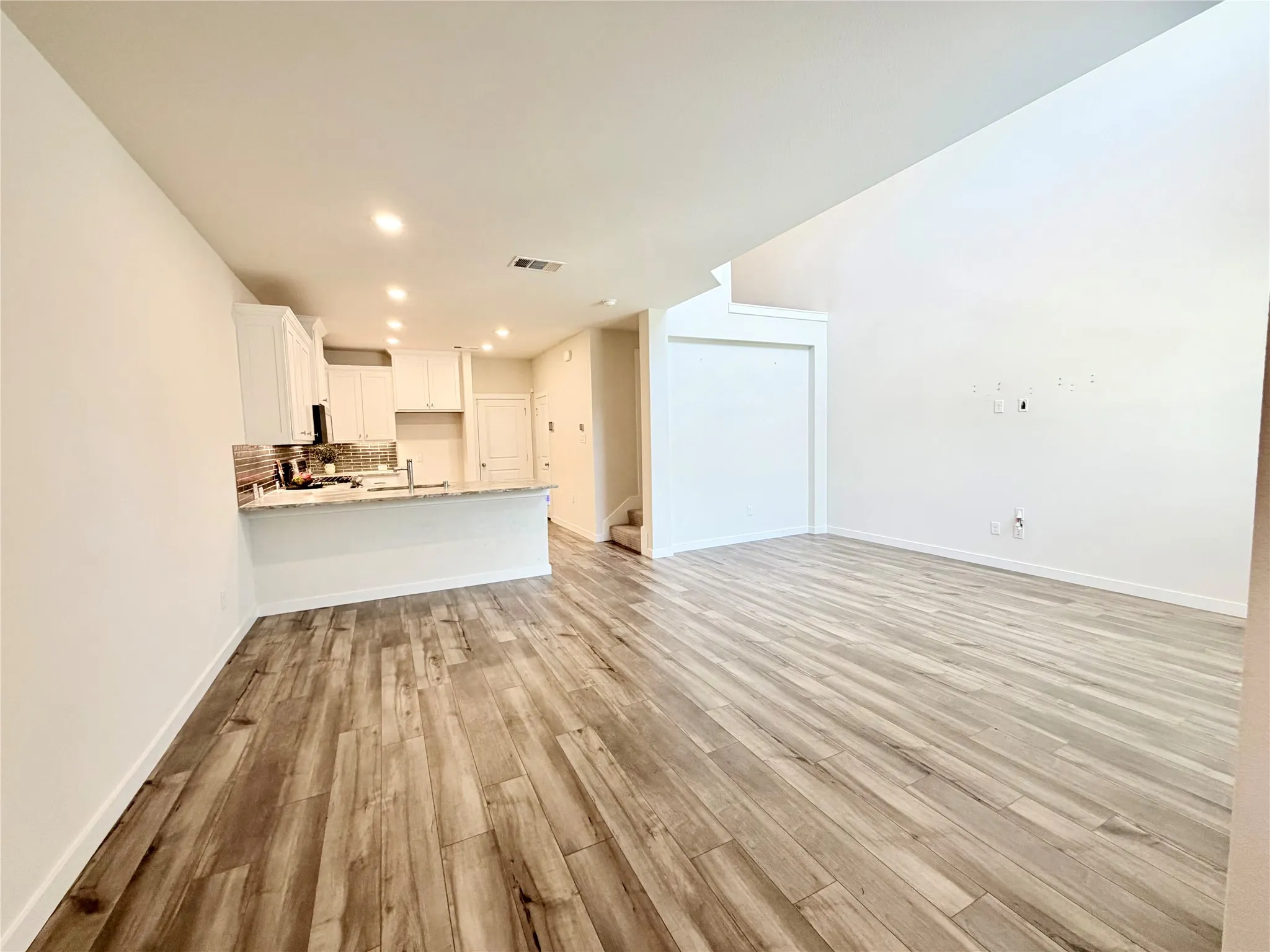 Open-concept living space featuring wood-finish flooring, a kitchen island with stone countertop, white shaker cabinetry, recessed lighting, and a vaulted ceiling